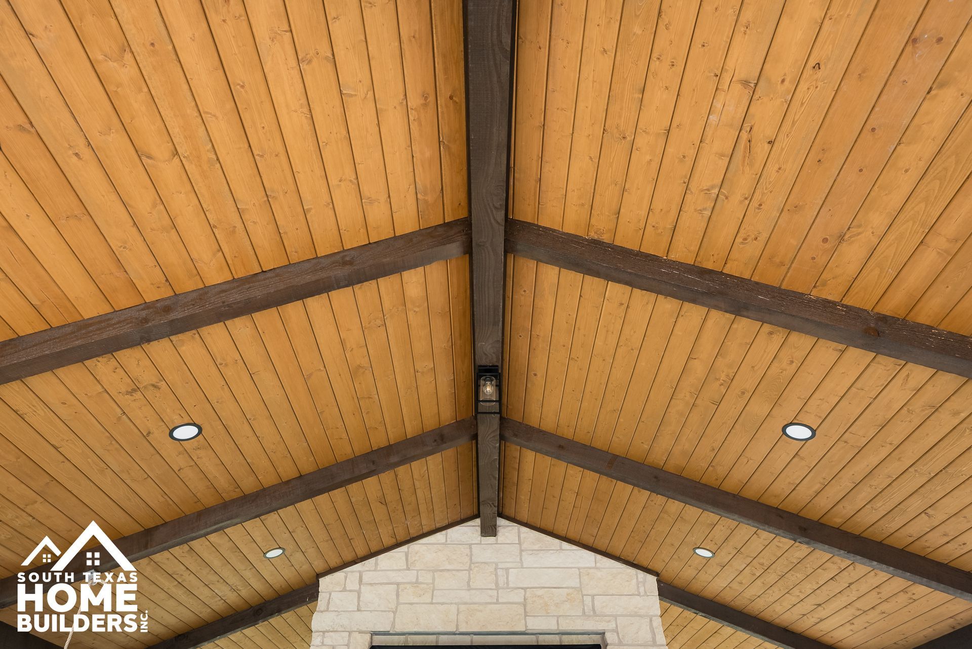 Wooden ceiling with exposed beams, recessed lighting, and stone fireplace below.
