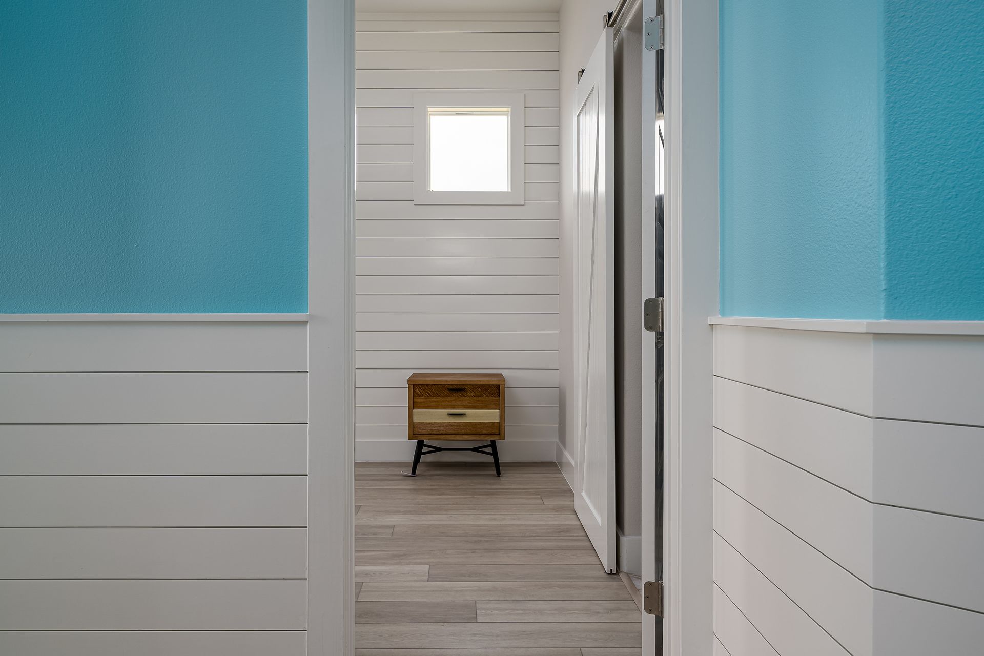 A hallway with blue and white walls and a wooden nightstand in the middle.