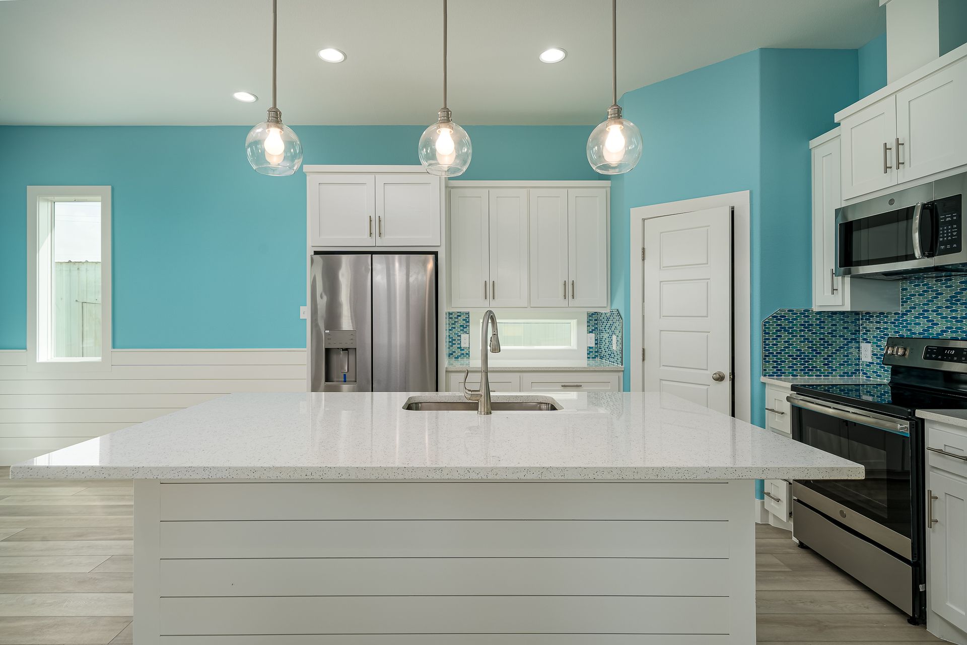 A kitchen with blue walls and white cabinets has a large island in the middle.