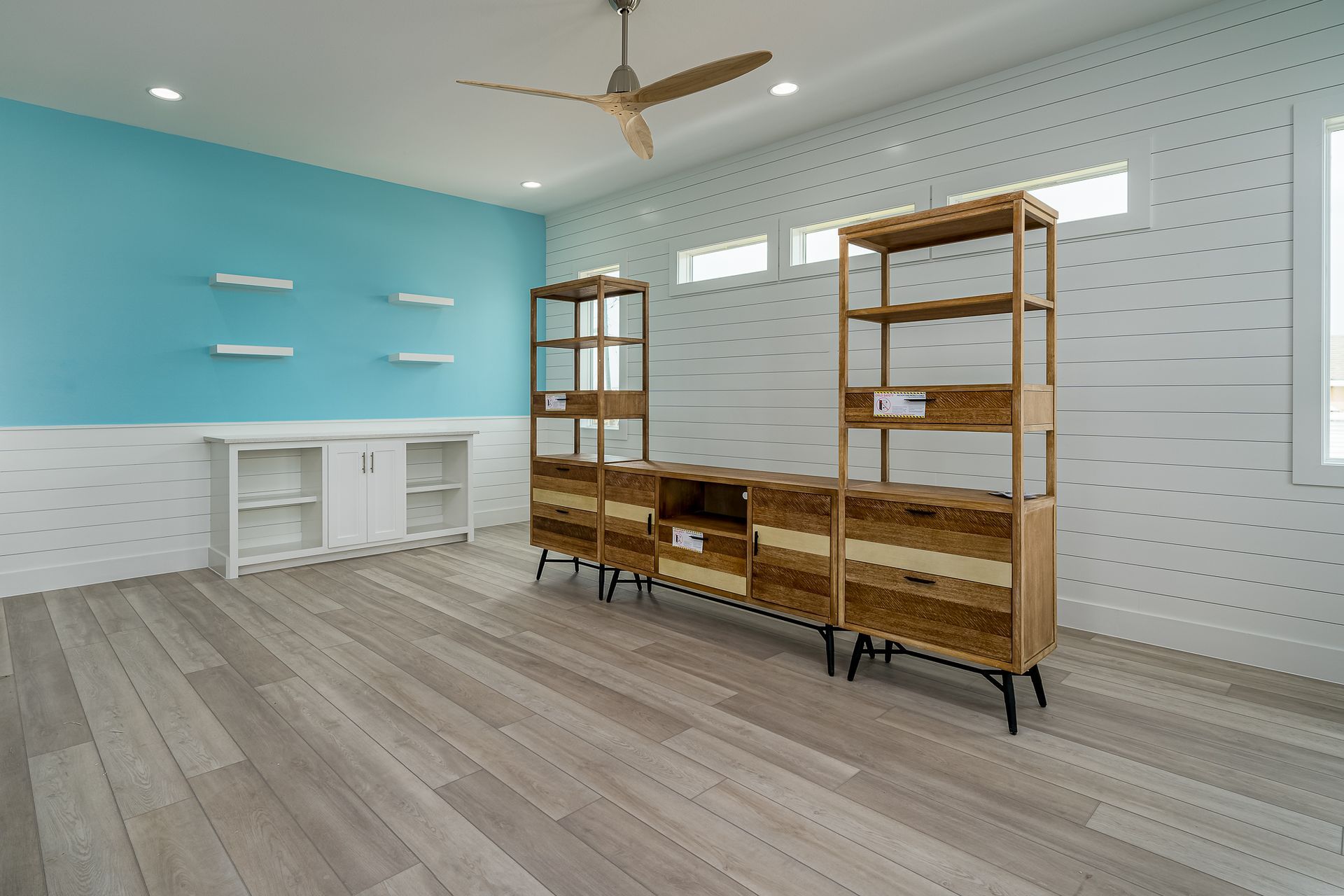 A living room with a blue wall , wooden shelves , and a ceiling fan.