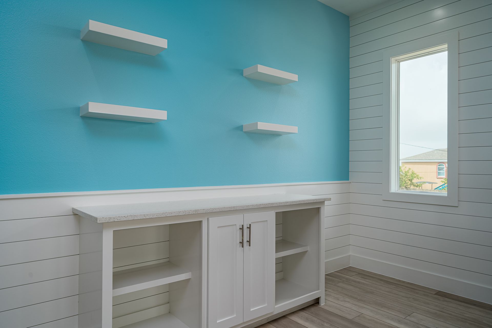 A room with blue walls and white shelves and a window.