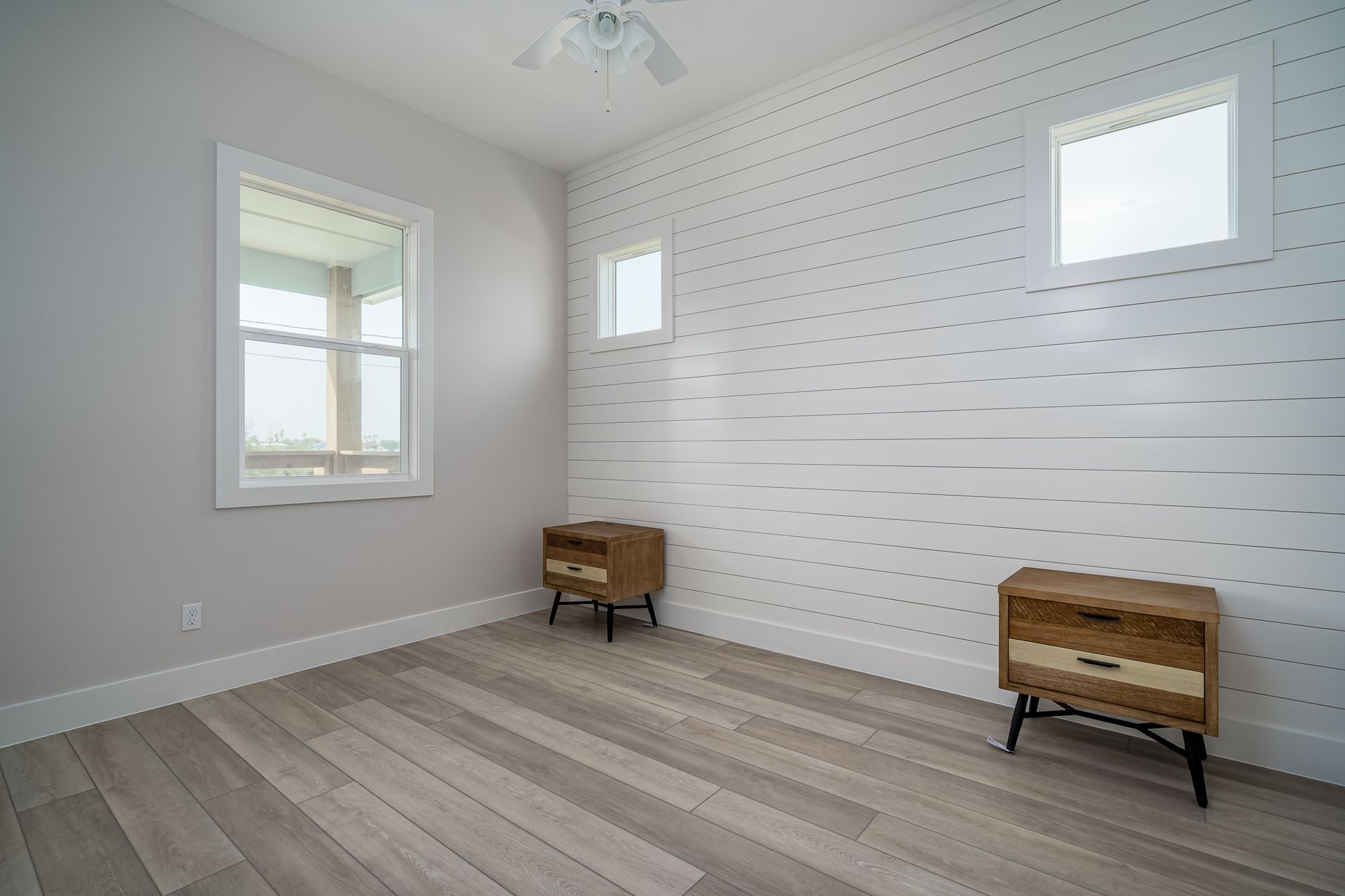 A bedroom with two nightstands , two windows and a ceiling fan.