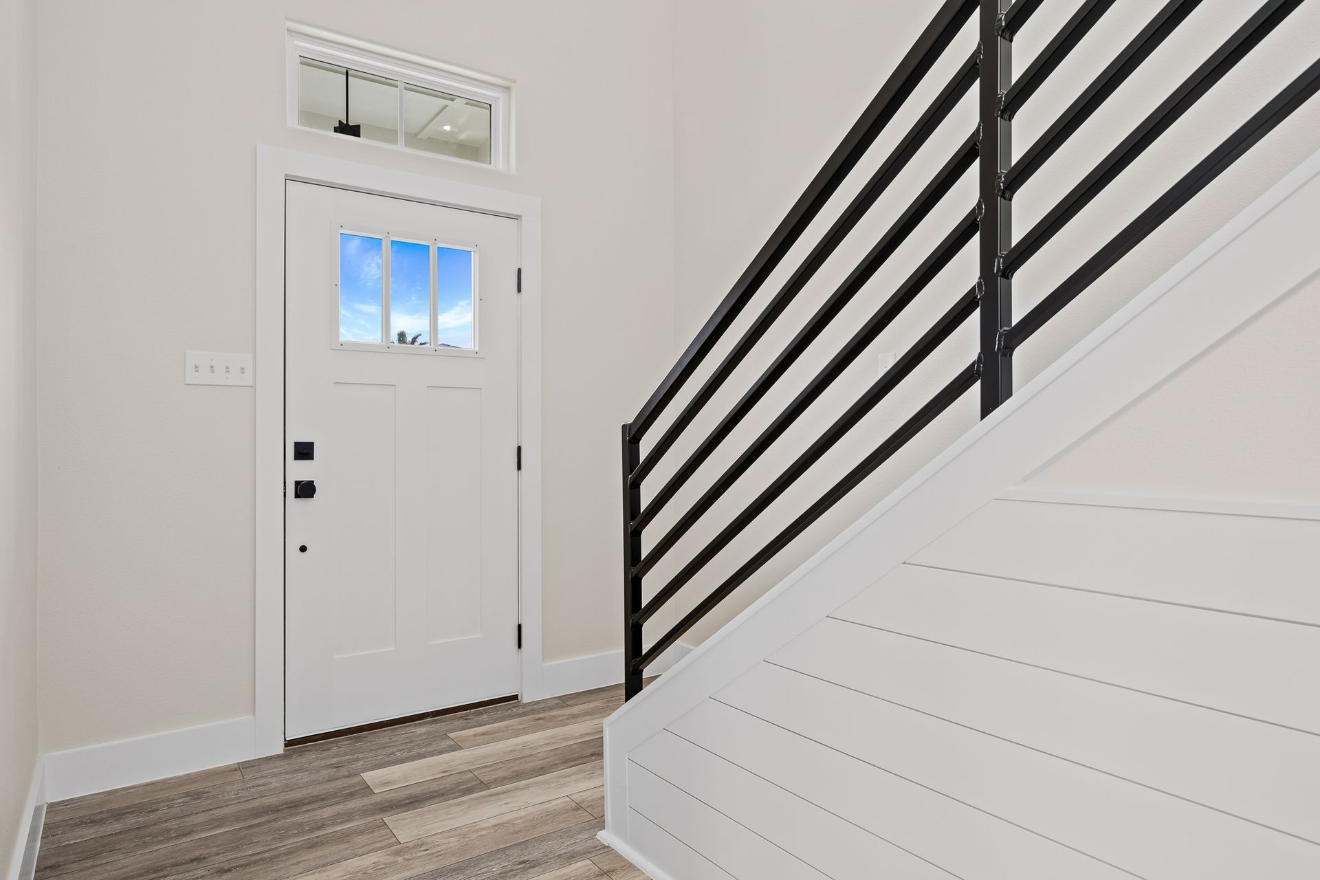 A hallway with stairs leading up to a white door and a black railing.