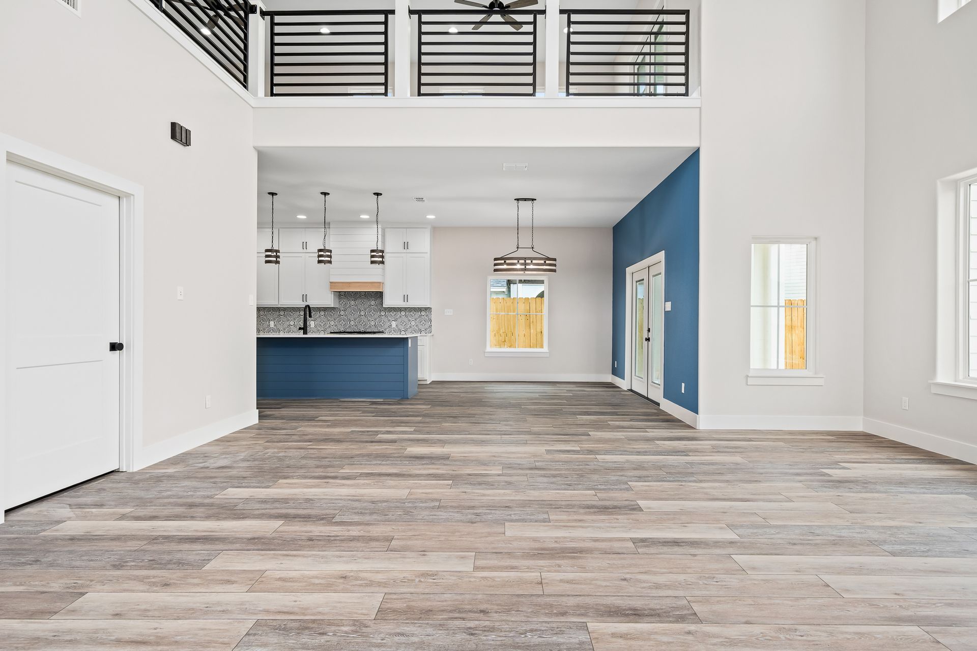 A large empty room with hardwood floors and a kitchen in the background.