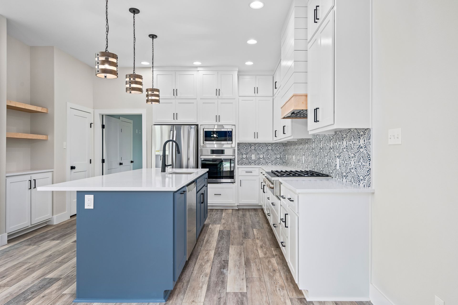 A kitchen with white cabinets , stainless steel appliances , and a blue island.