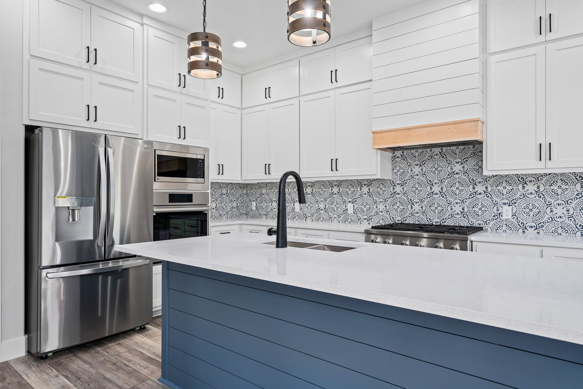 A kitchen with white cabinets , stainless steel appliances , and a blue island.