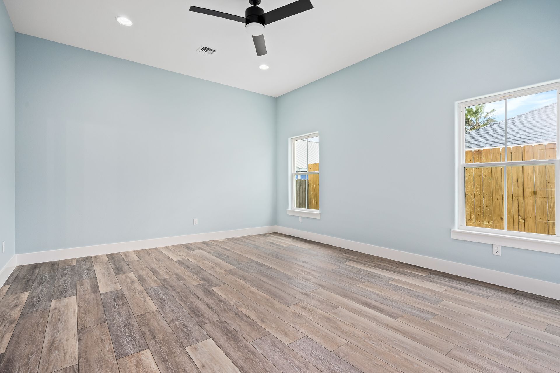 An empty room with a ceiling fan and two windows.