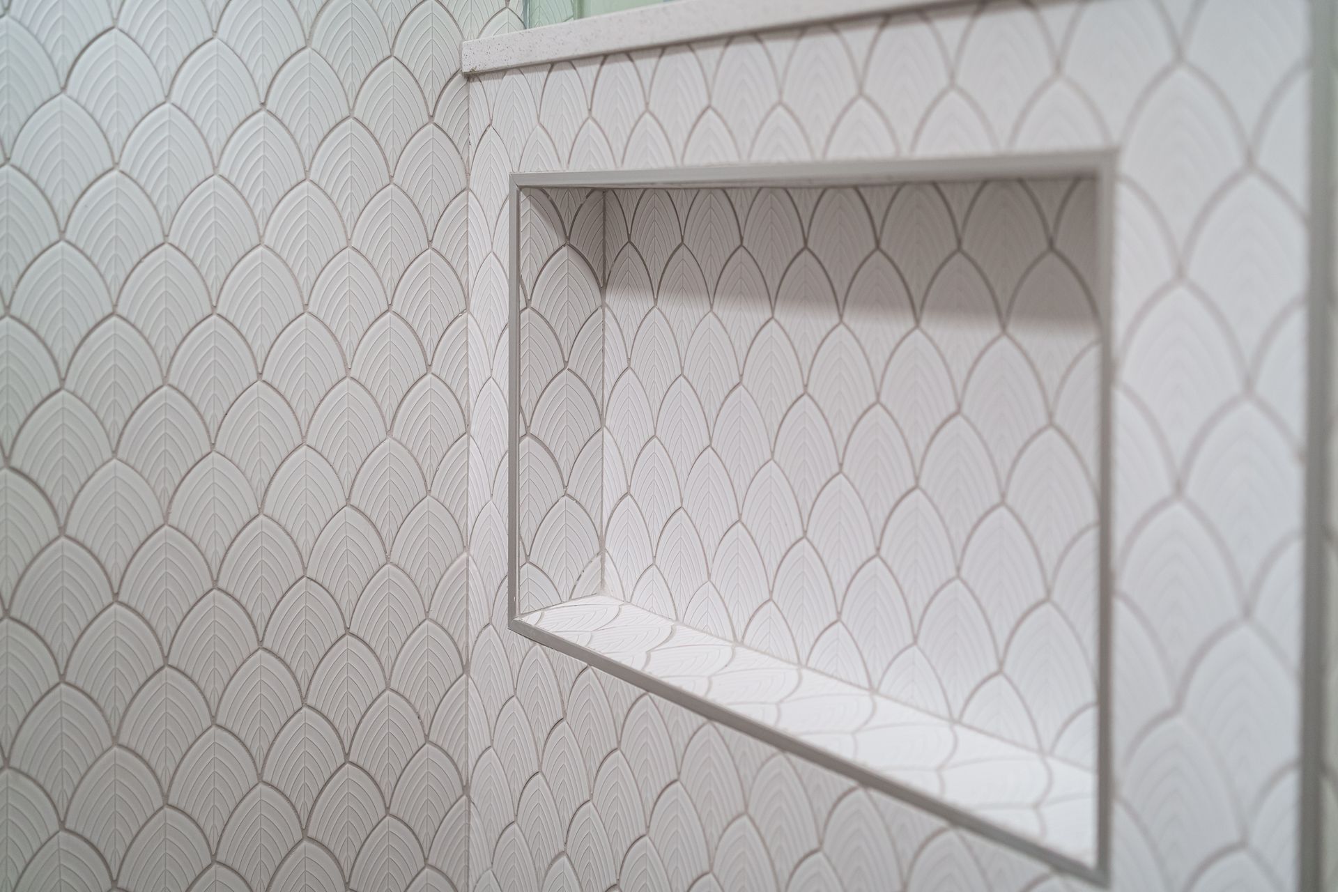 A shower niche in a bathroom with white tiles and a shelf.