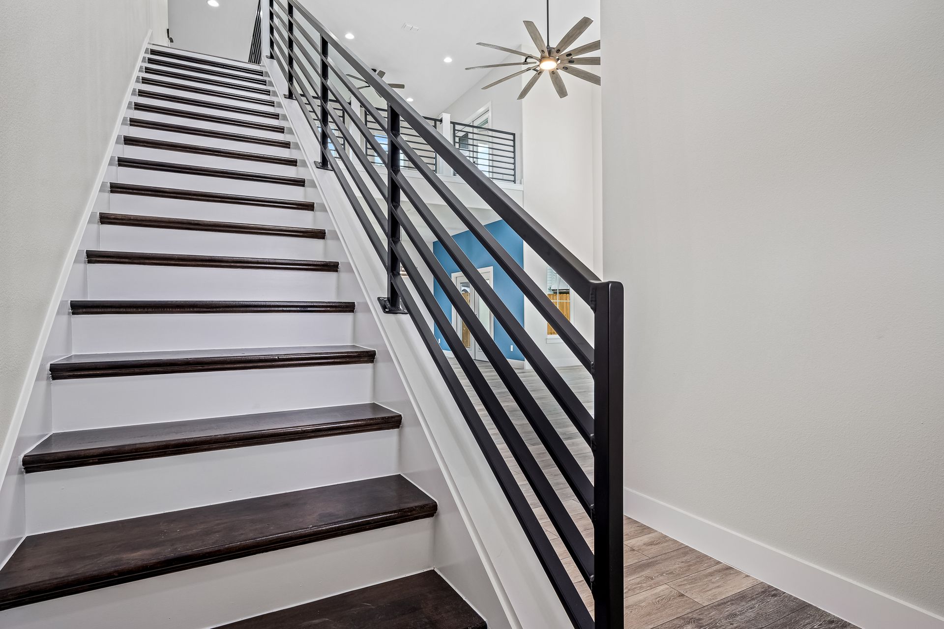 A set of stairs with a black railing and a ceiling fan.
