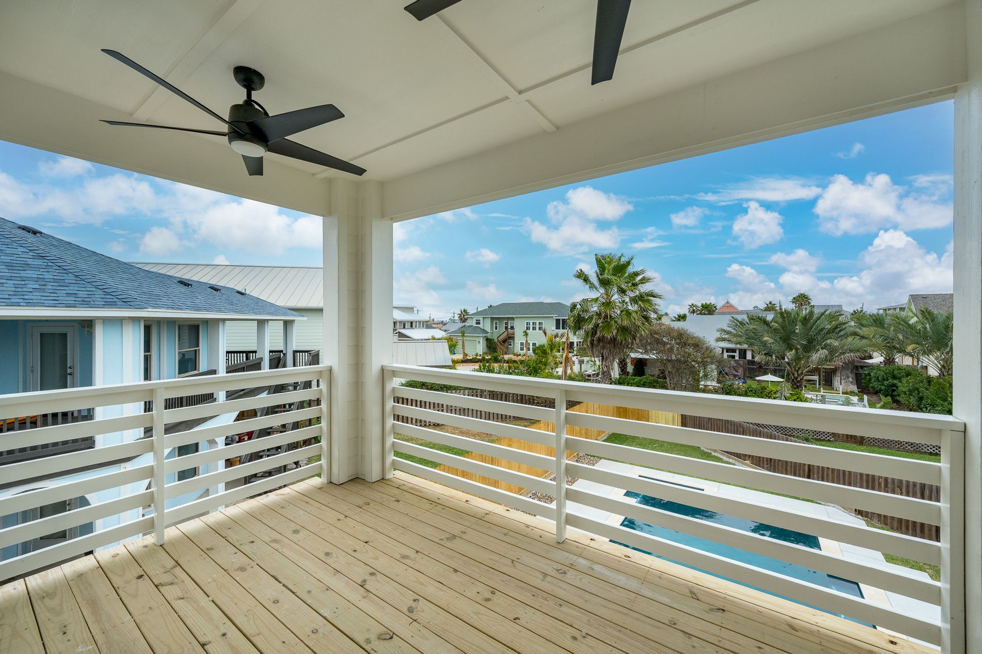 A balcony with a ceiling fan and a view of a house and a pool.