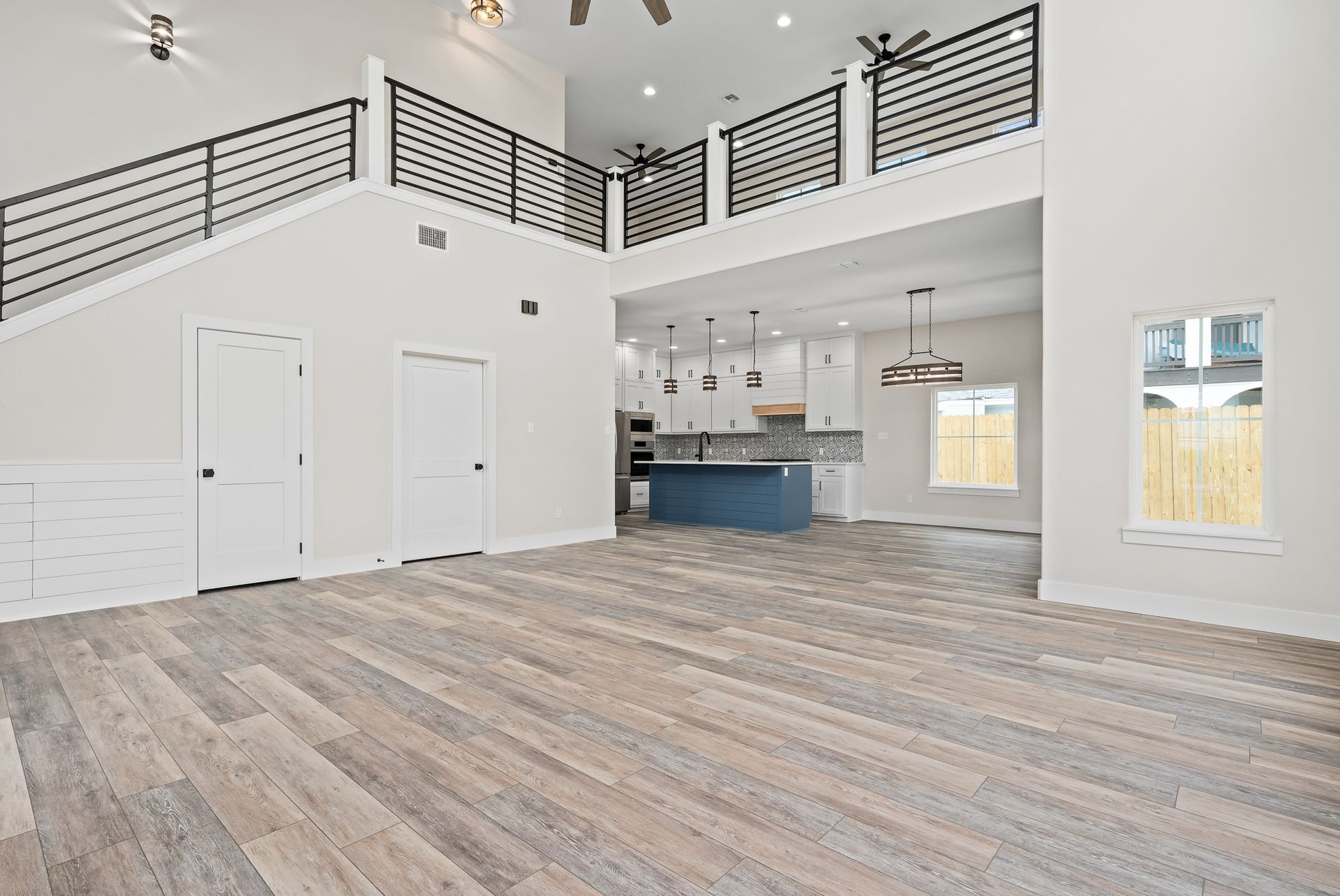 A large empty room with a wooden floor and stairs leading to a kitchen.
