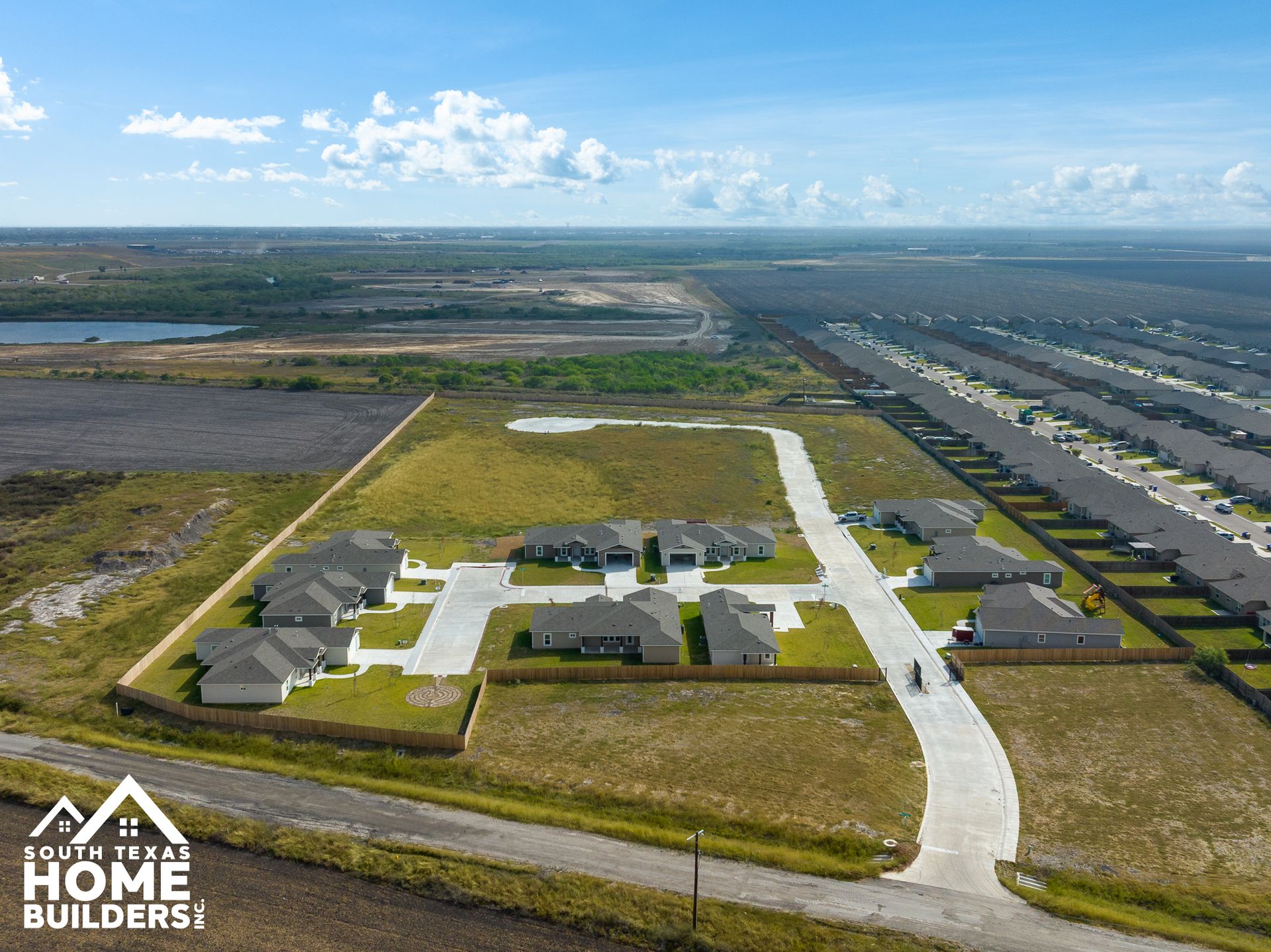 Aerial view of houses on a new road in a developing area; green grass, gray homes, bright sky.