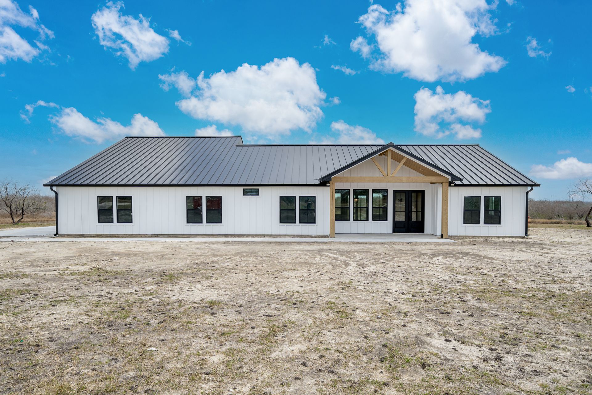 A large white house with a black roof is sitting in the middle of a field.