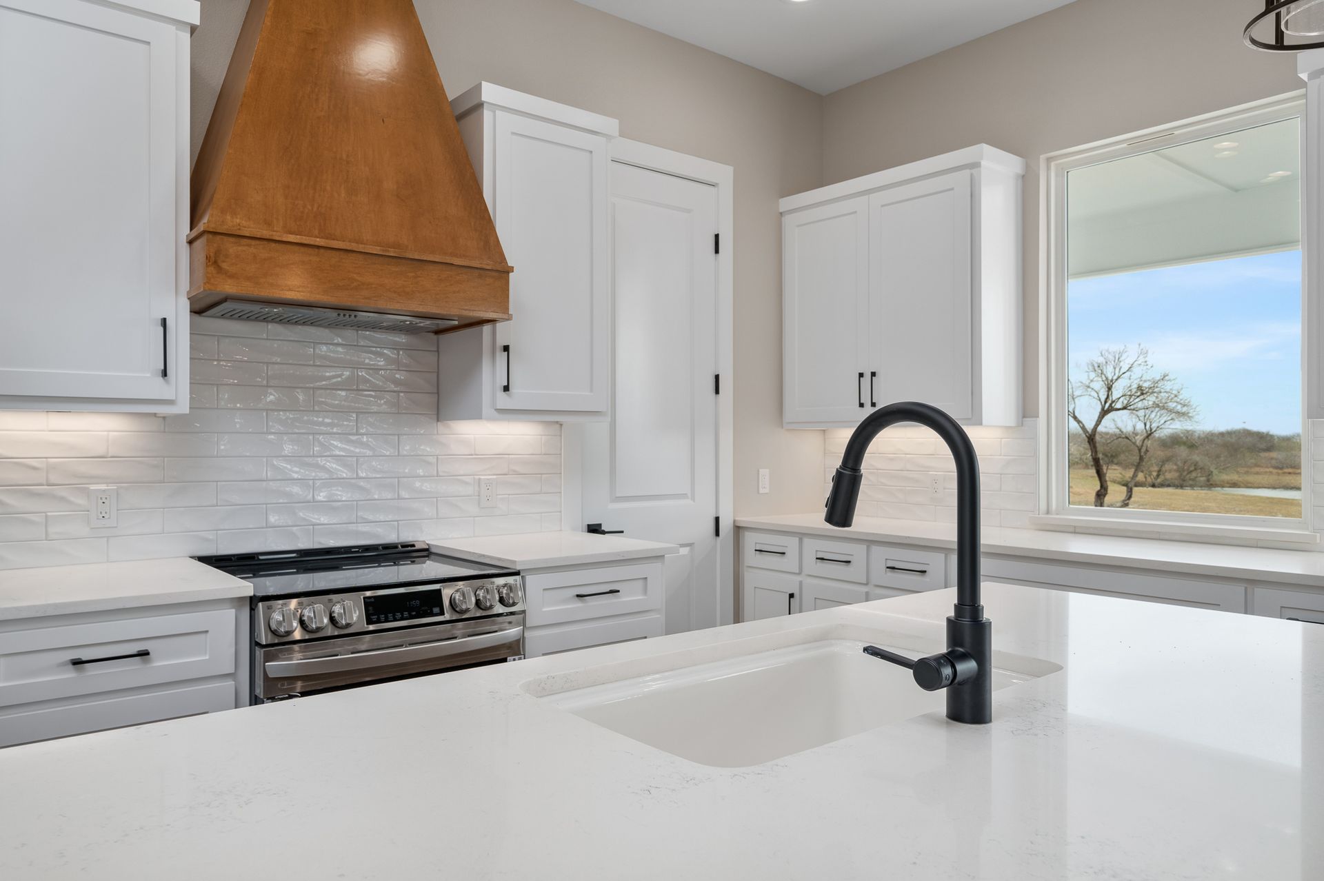 A kitchen with white cabinets , a stove , a sink and a window.