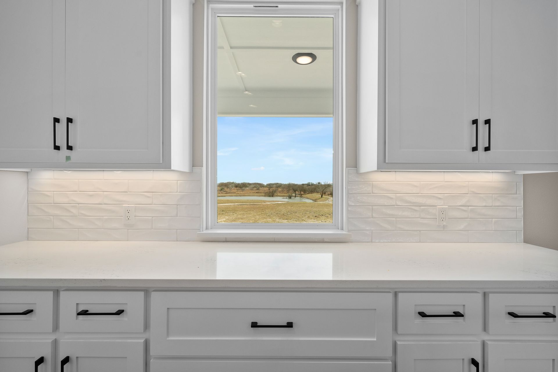 A kitchen with white cabinets and a window over the sink.