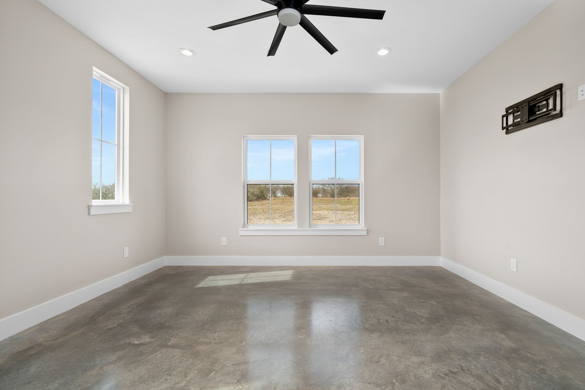 An empty room with a ceiling fan and two windows.