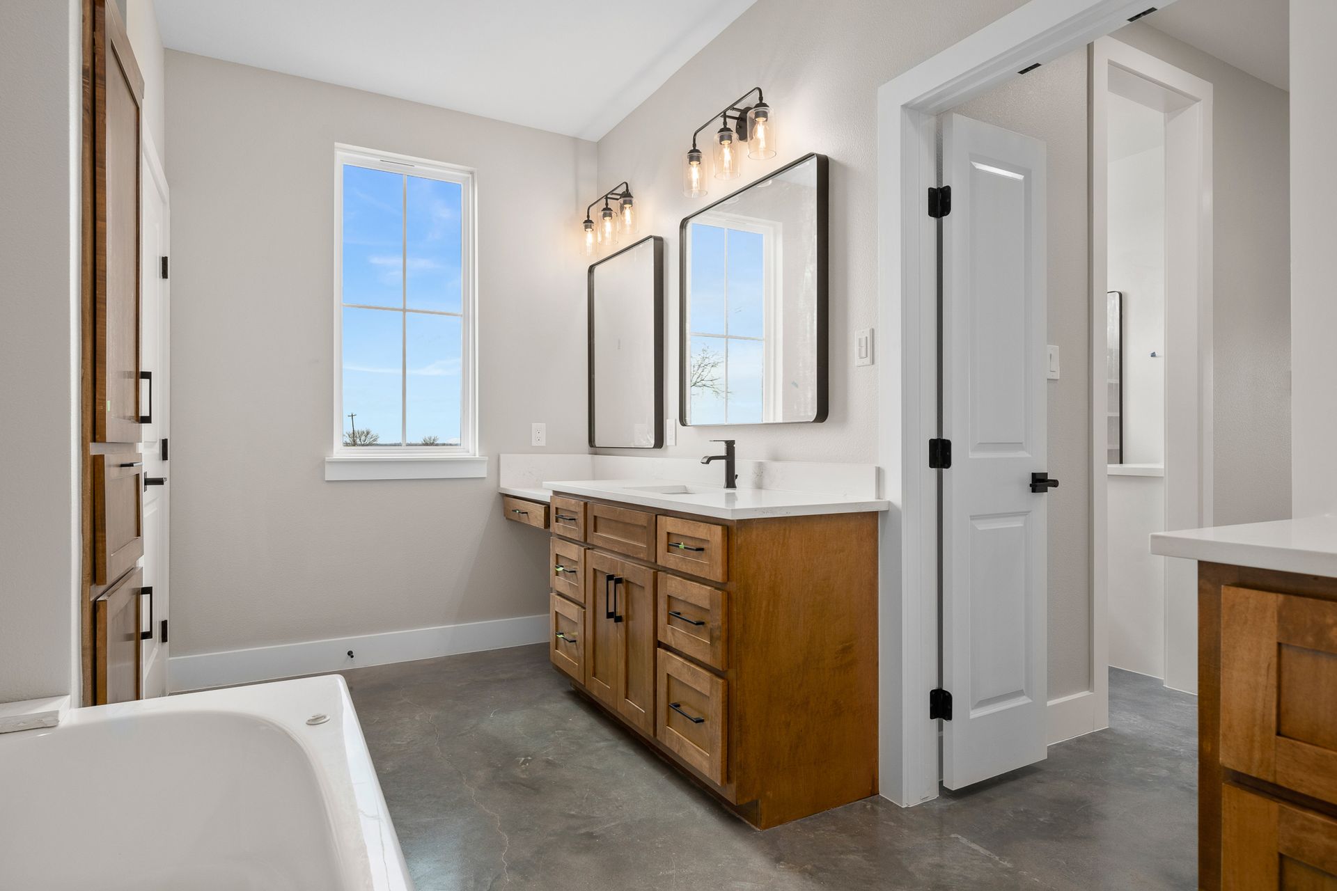 A bathroom with two sinks , two mirrors , a tub and a window.