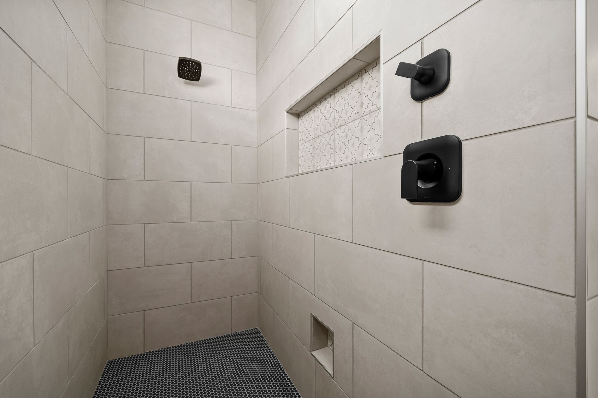 A shower with a black and white tile floor and a black shower head.