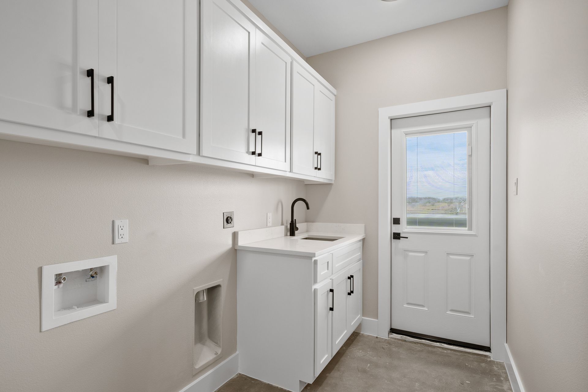 A laundry room with white cabinets , a sink , and a window.