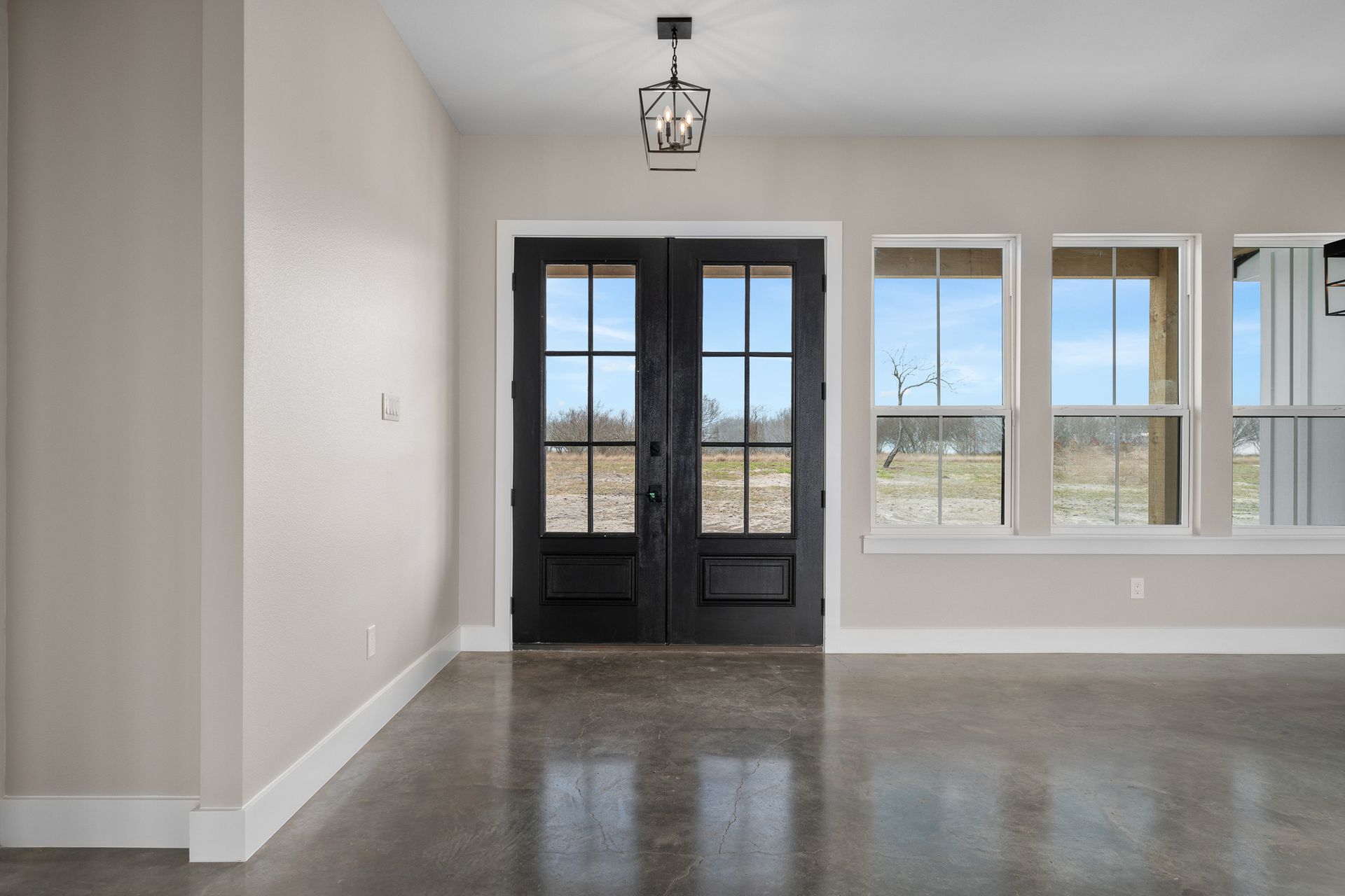 An empty living room with a black door and windows.