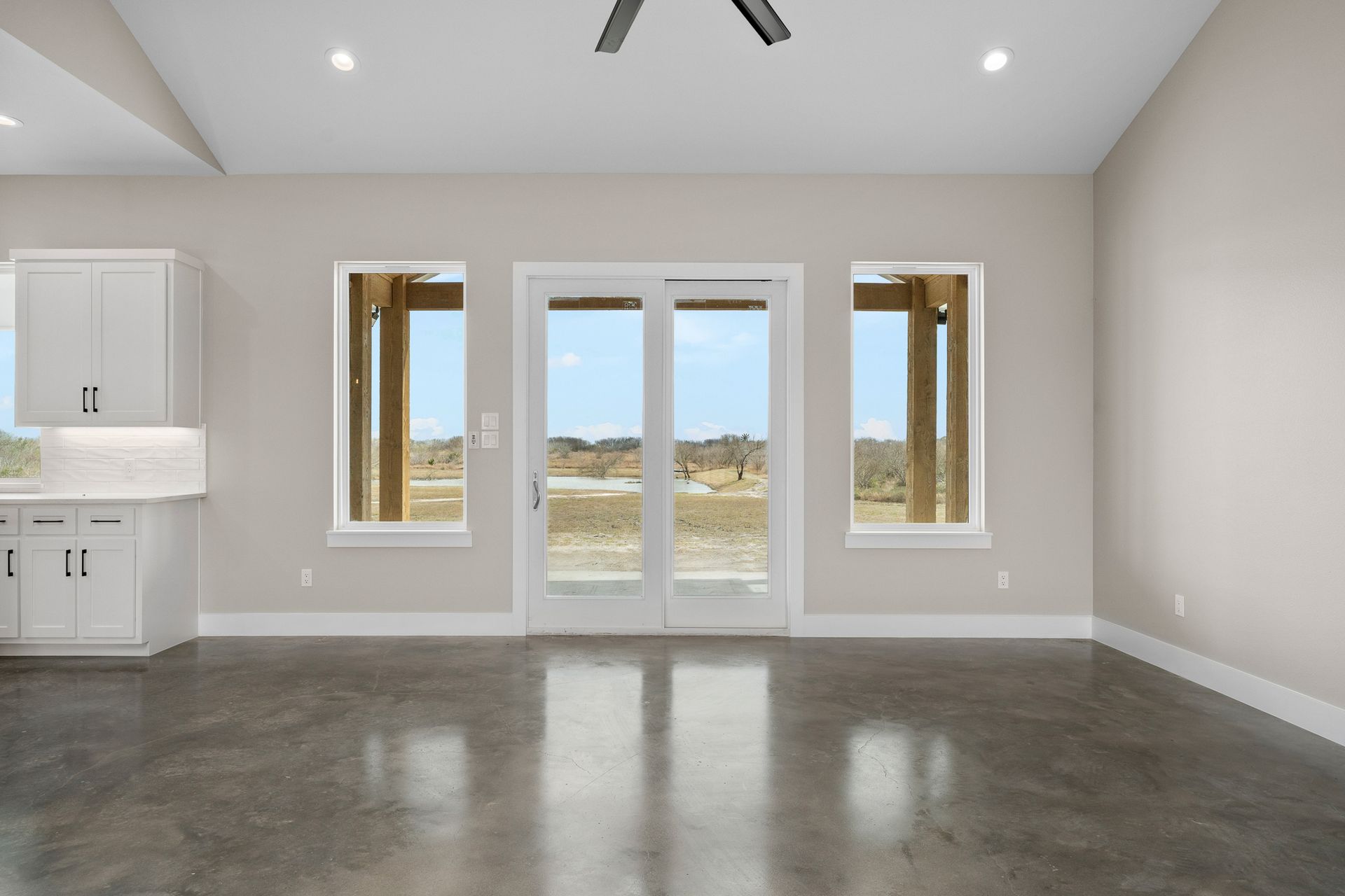An empty room with a ceiling fan and sliding glass doors.