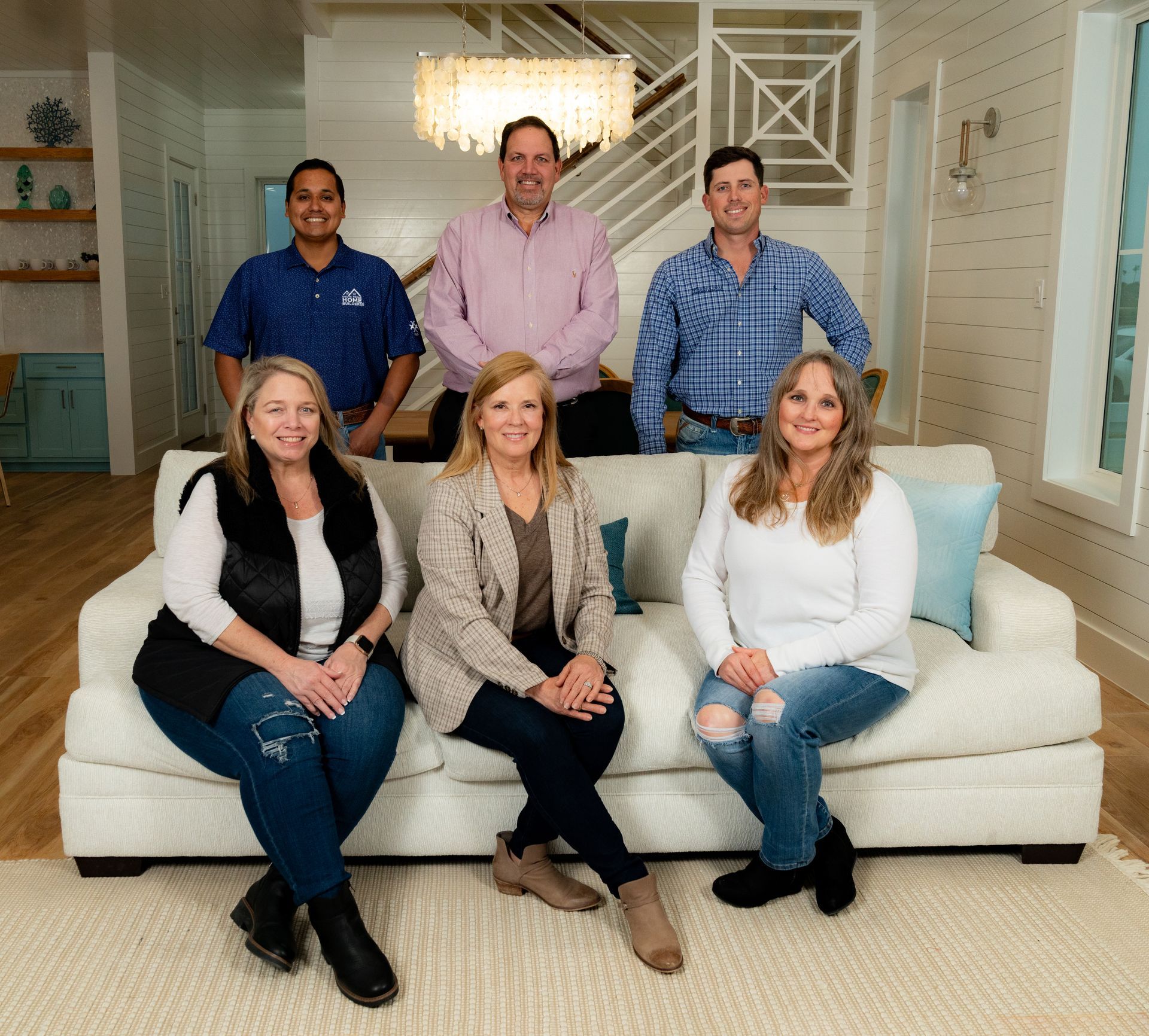 Group of six people posing for a photo in a living room; three standing behind a seated group of three.