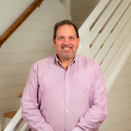 A man in a pink shirt is standing in front of a white staircase.