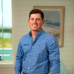 A man in a blue plaid shirt is standing in front of a window.