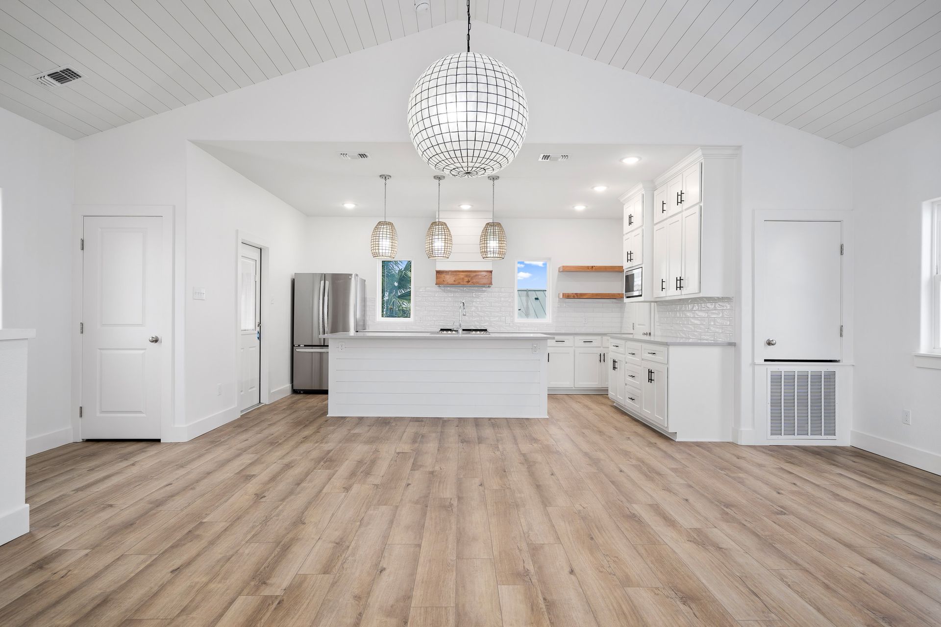 A large empty kitchen with hardwood floors and white cabinets.