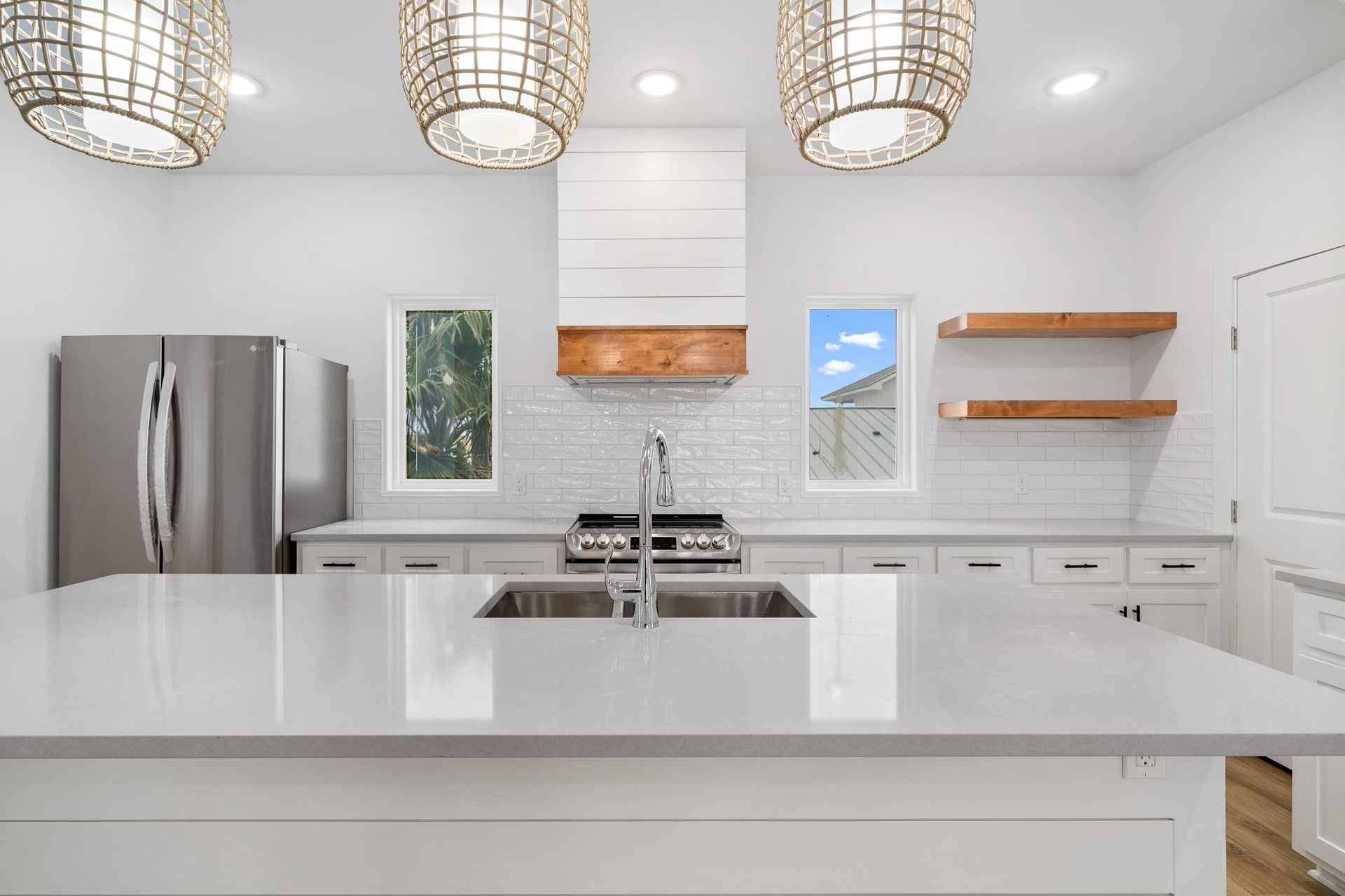 A kitchen with white cabinets , stainless steel appliances , a sink and a refrigerator.