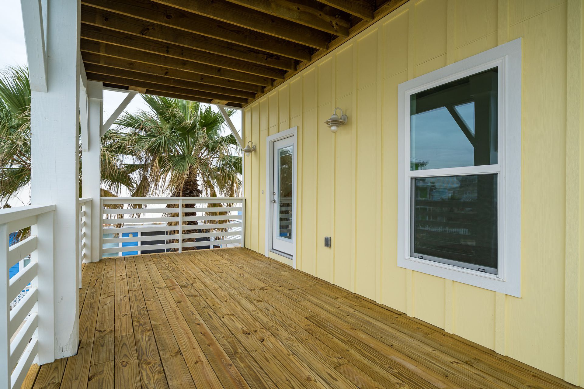 A porch with a wooden floor and a yellow house in the background