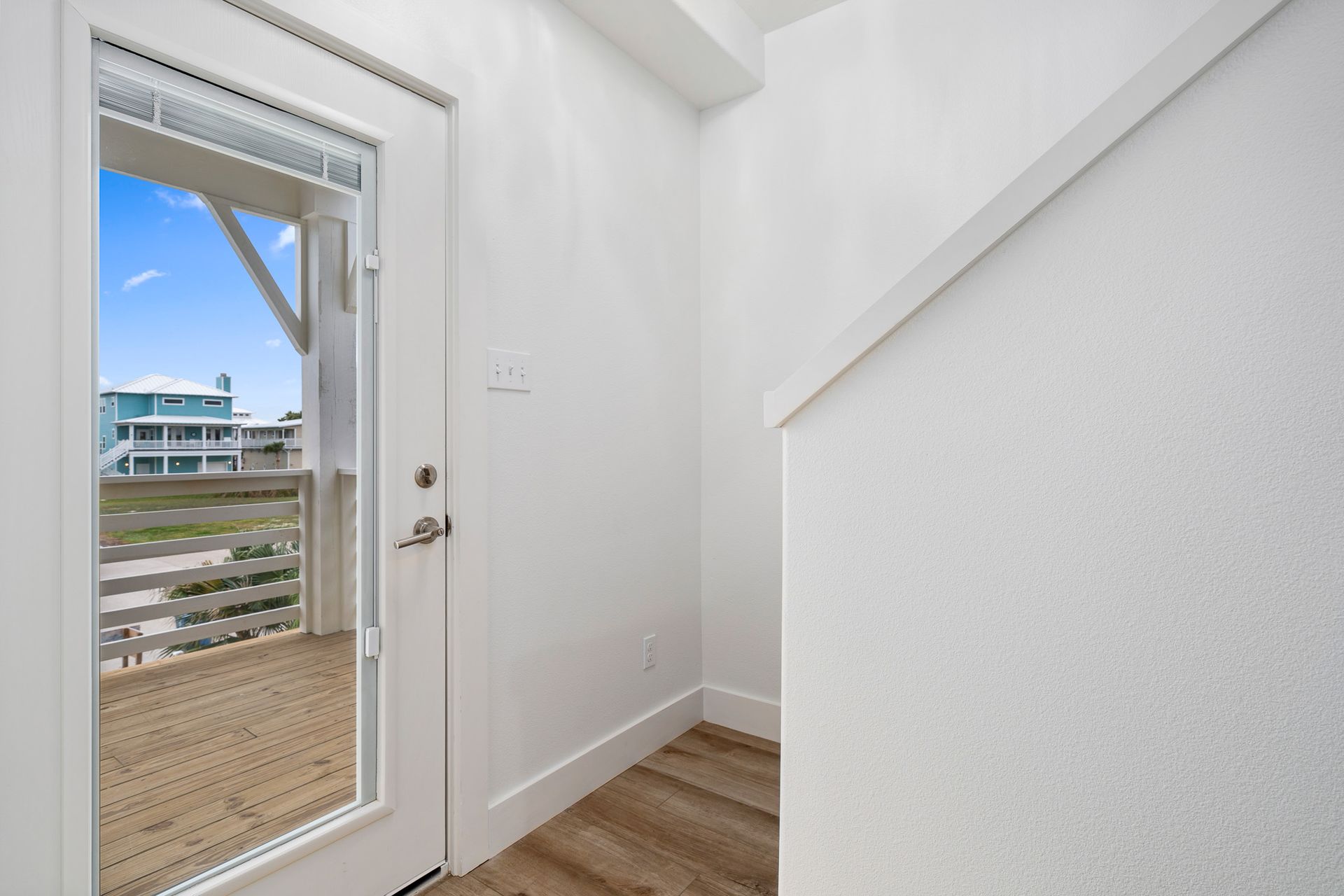 A hallway with stairs and a door leading to a balcony.