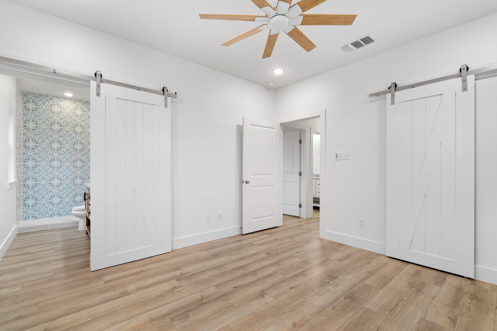 An empty bedroom with sliding barn doors and a ceiling fan.