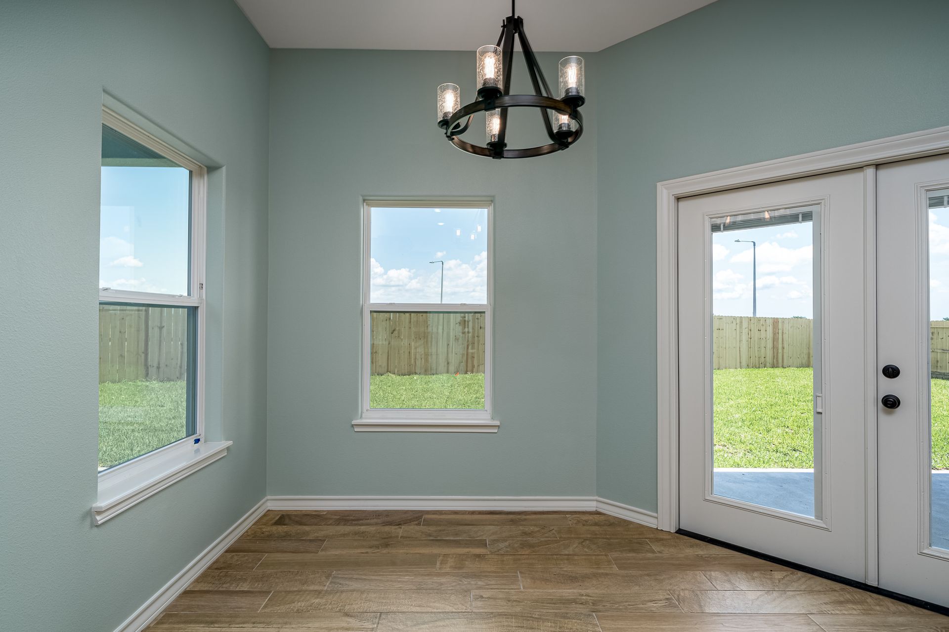 An empty room with a chandelier hanging from the ceiling and two windows.