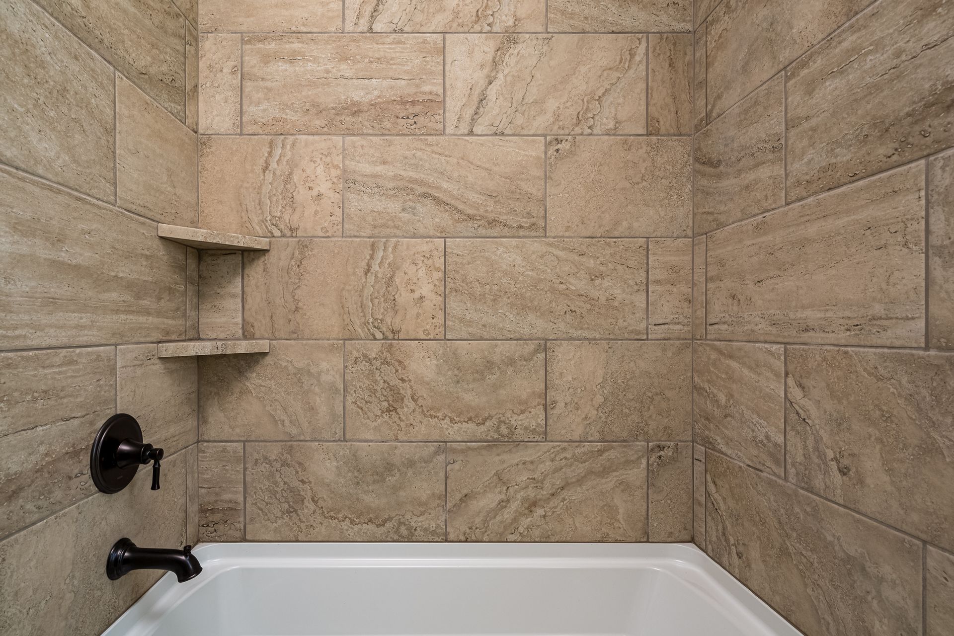 A bathroom with a tub and a shower with tiled walls.