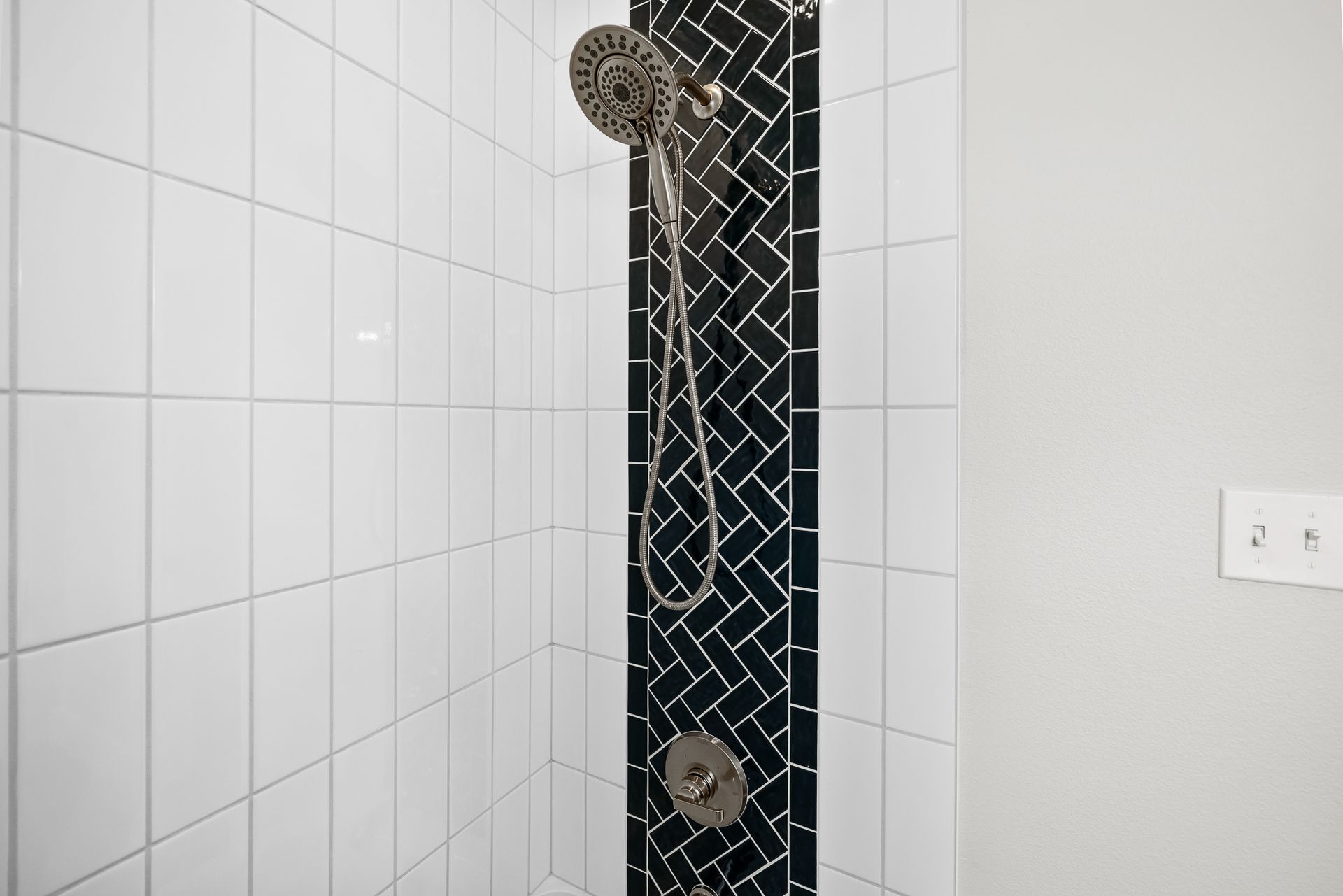A shower with a black and white tile border and a shower head.