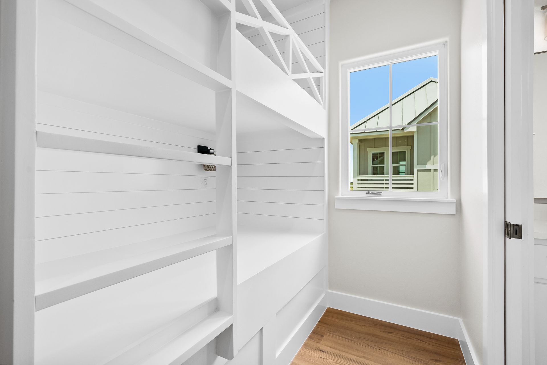 A walk in closet with white shelves and a window.