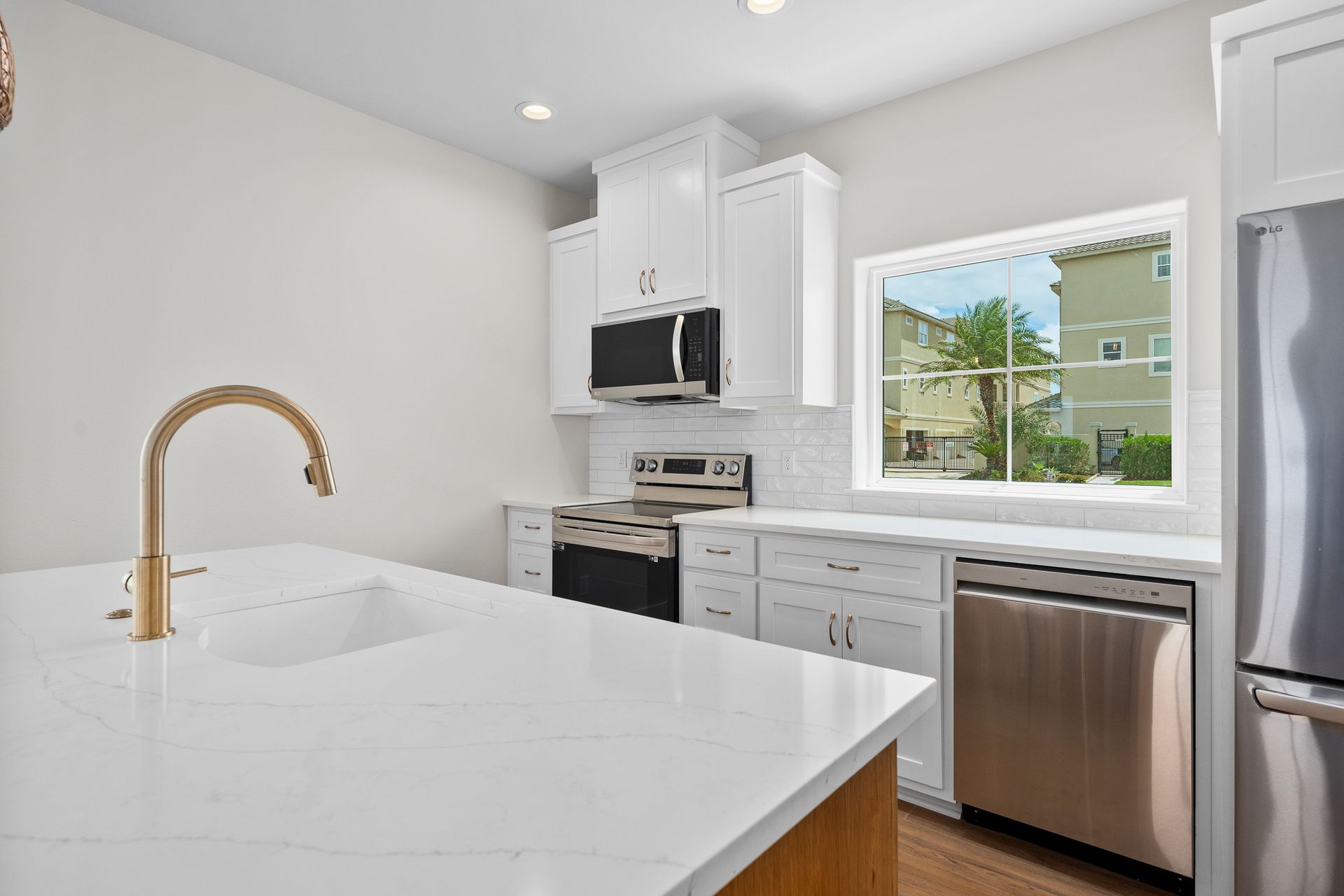 A kitchen with white cabinets , stainless steel appliances , a sink , and a window.