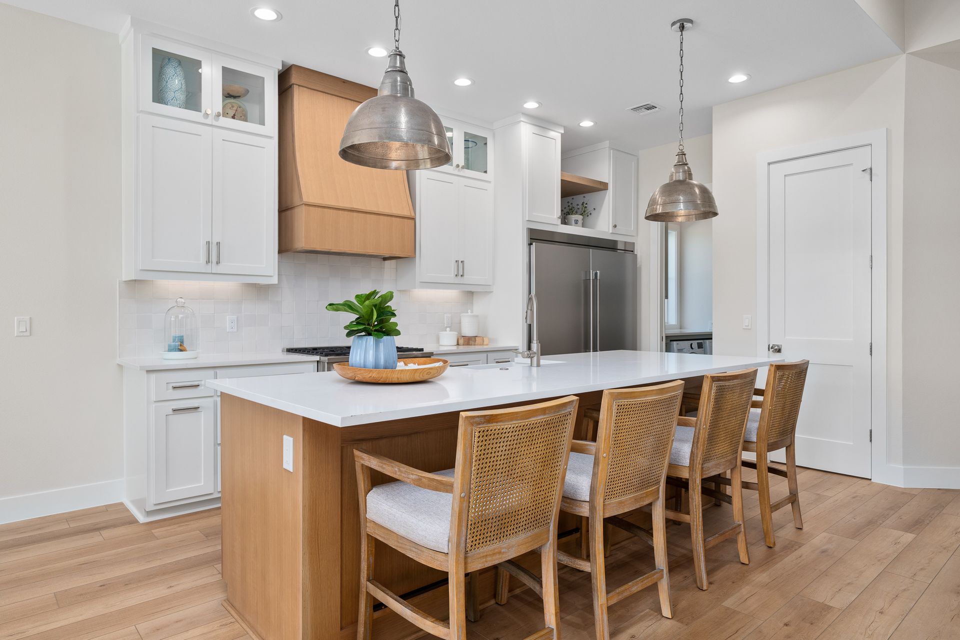 A kitchen with white cabinets , a large island , and wicker chairs.