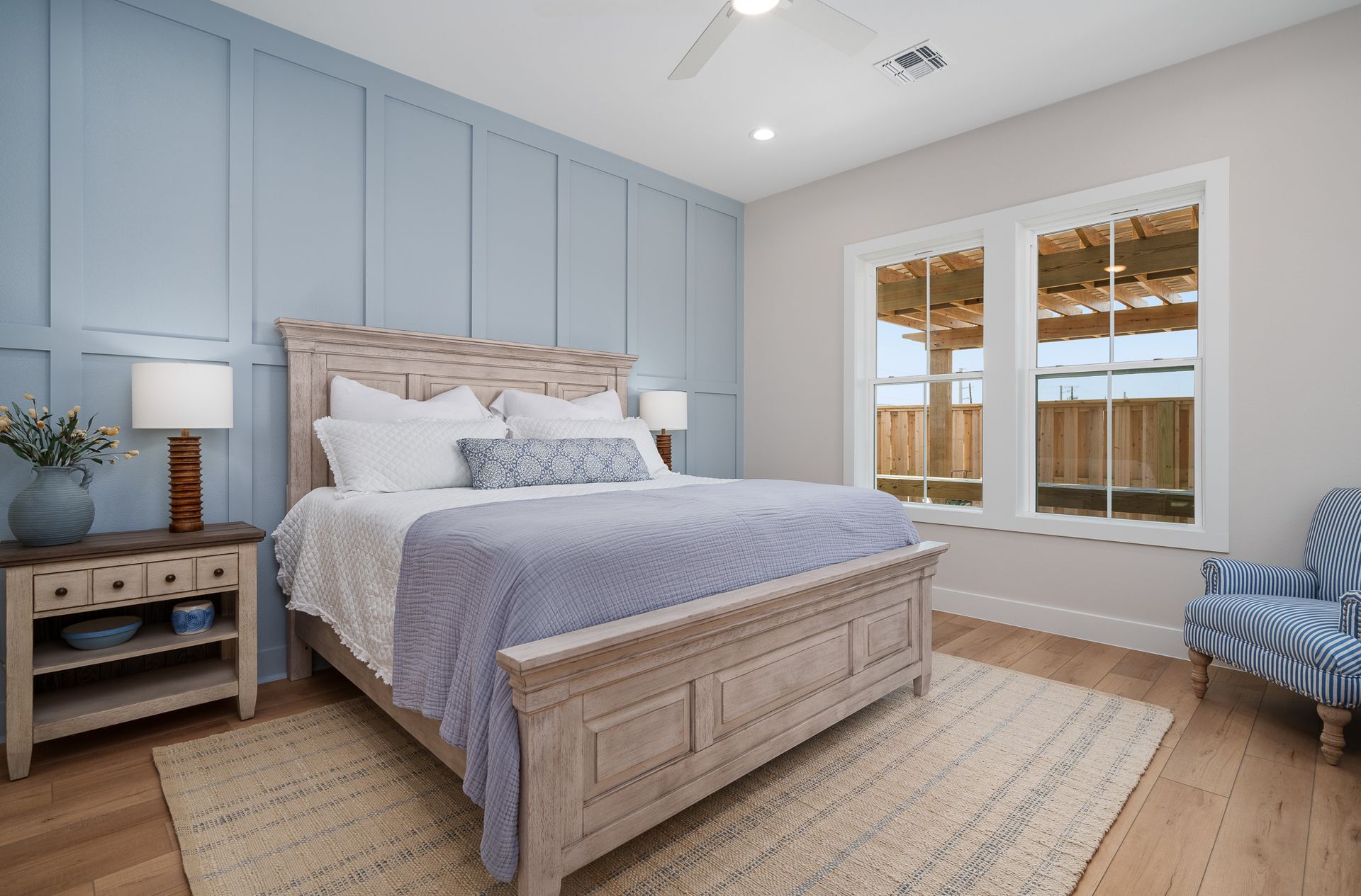 A bedroom with a bed , nightstand , chair and two windows.