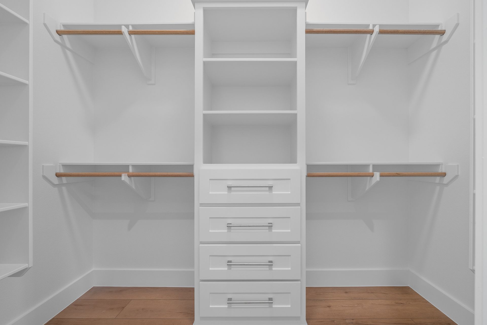 An empty walk in closet with white shelves and drawers.