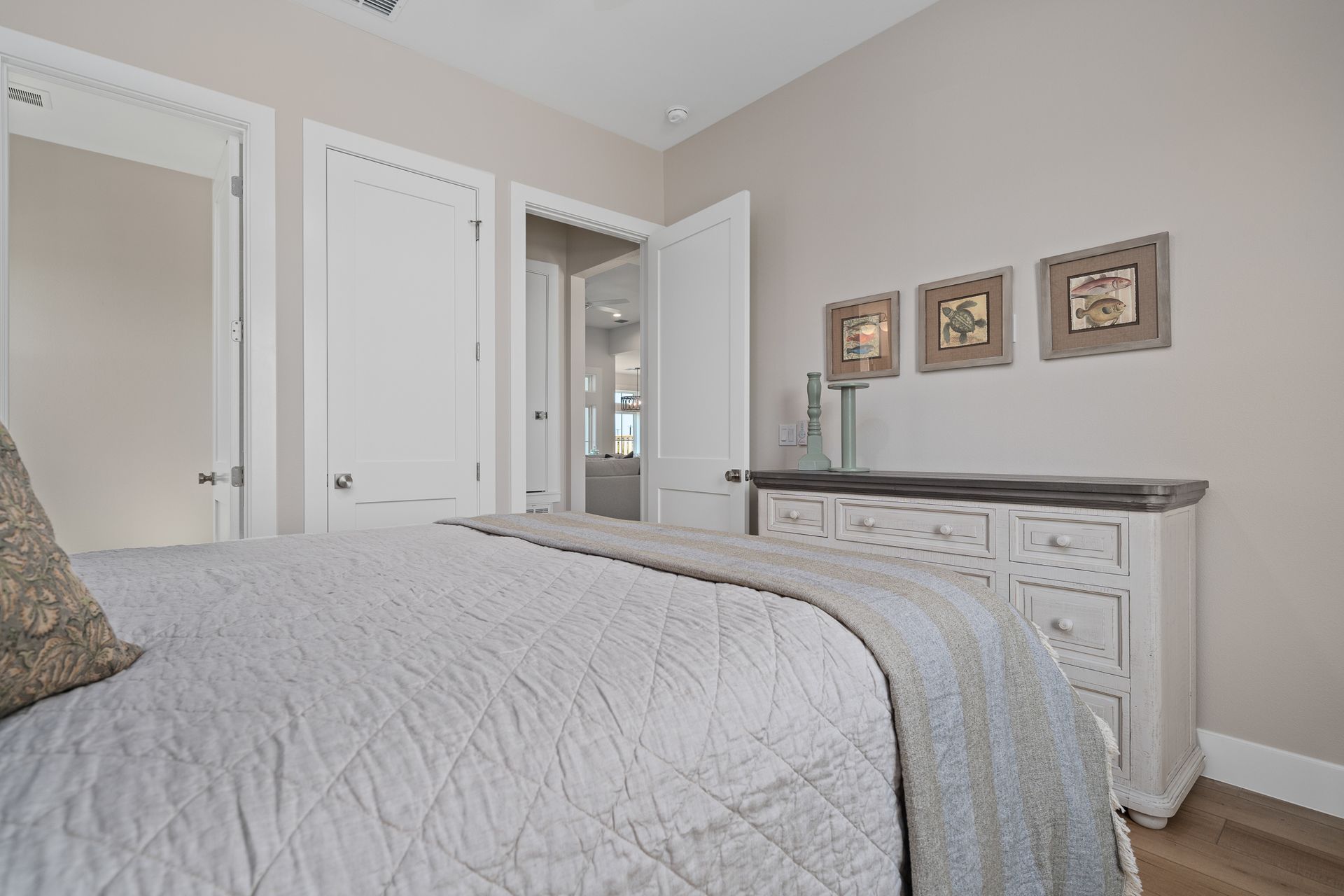 A bedroom with a bed , dresser , and paintings on the wall.