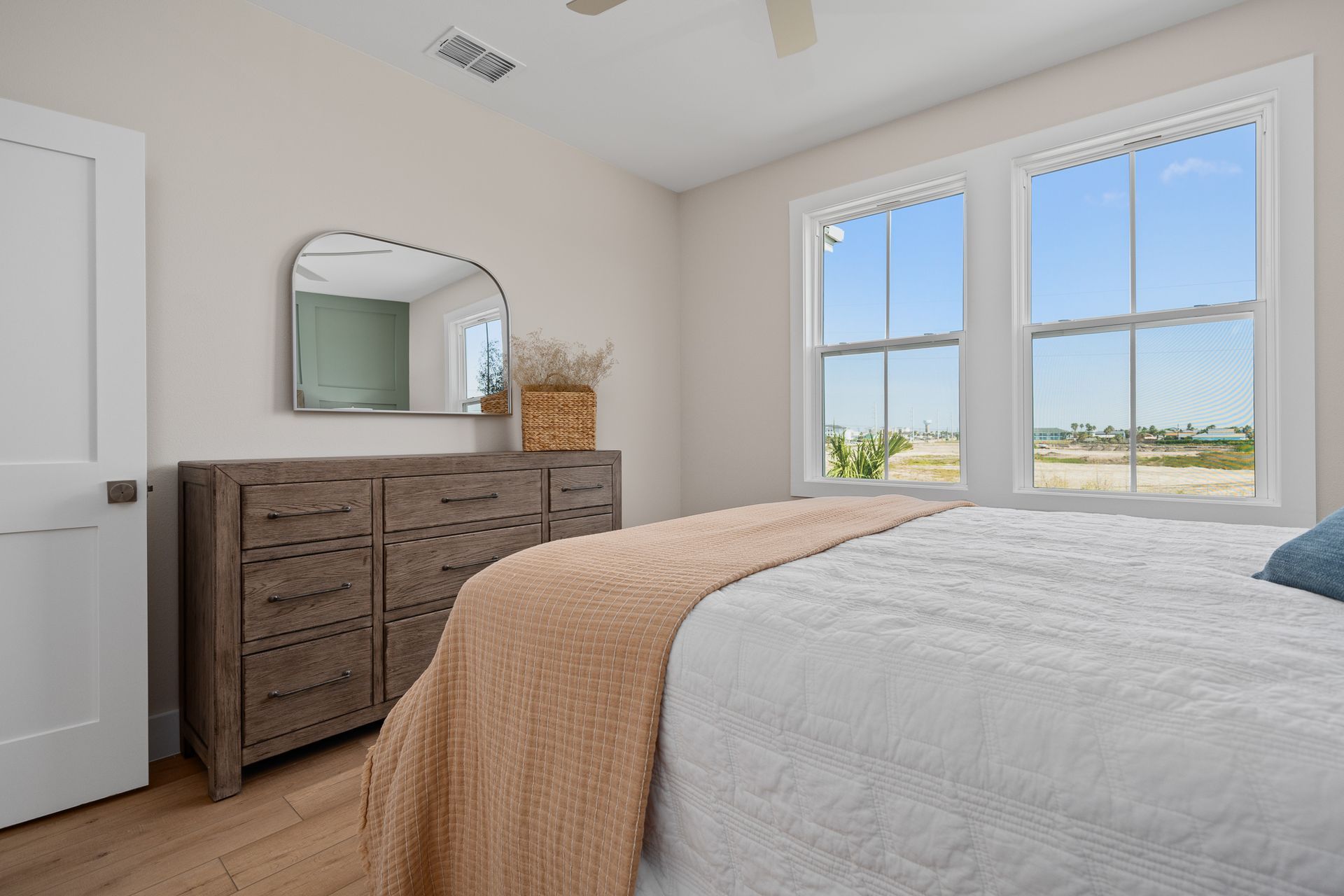 A bedroom with a bed , dresser , mirror and two windows.