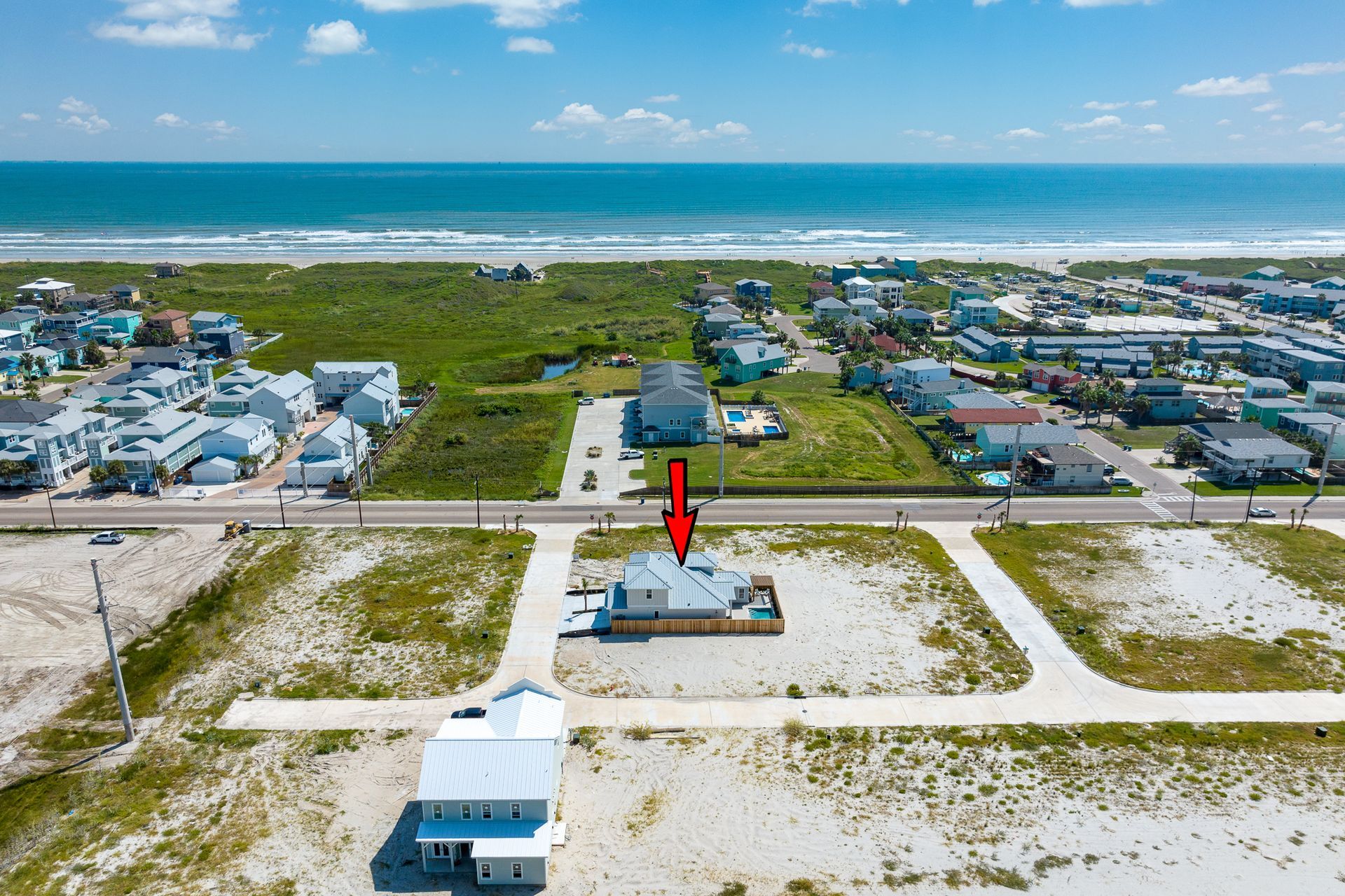 An aerial view of a house on the beach with a red arrow pointing to it.