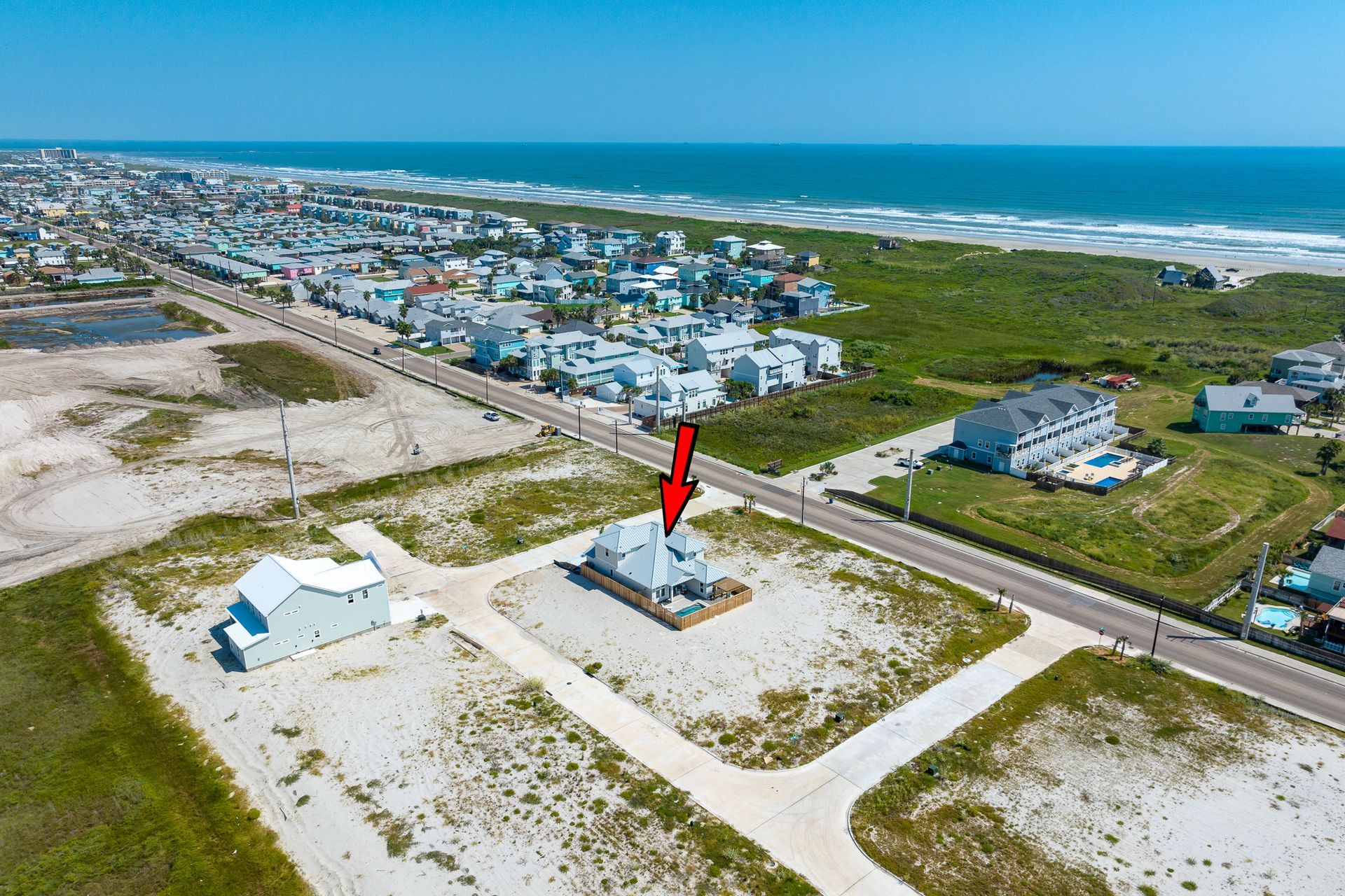 An aerial view of a house on the beach with a red arrow pointing to it.