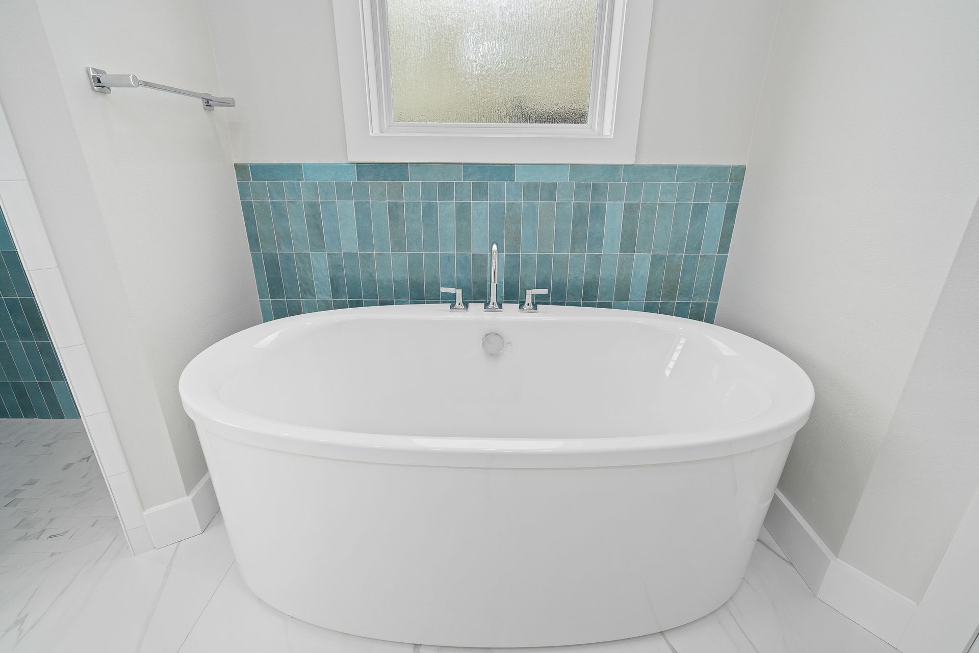 A bathtub in a bathroom with blue tiles and a window.