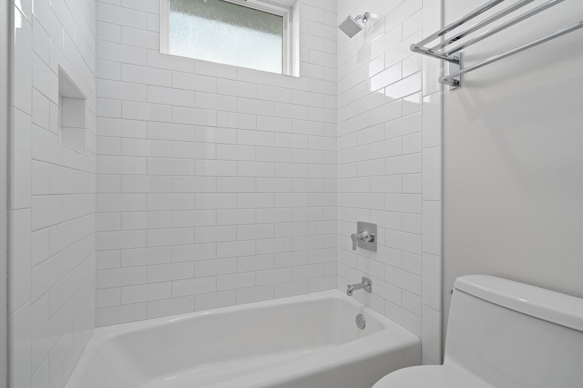 A bathroom with a tub , toilet , shower and window.