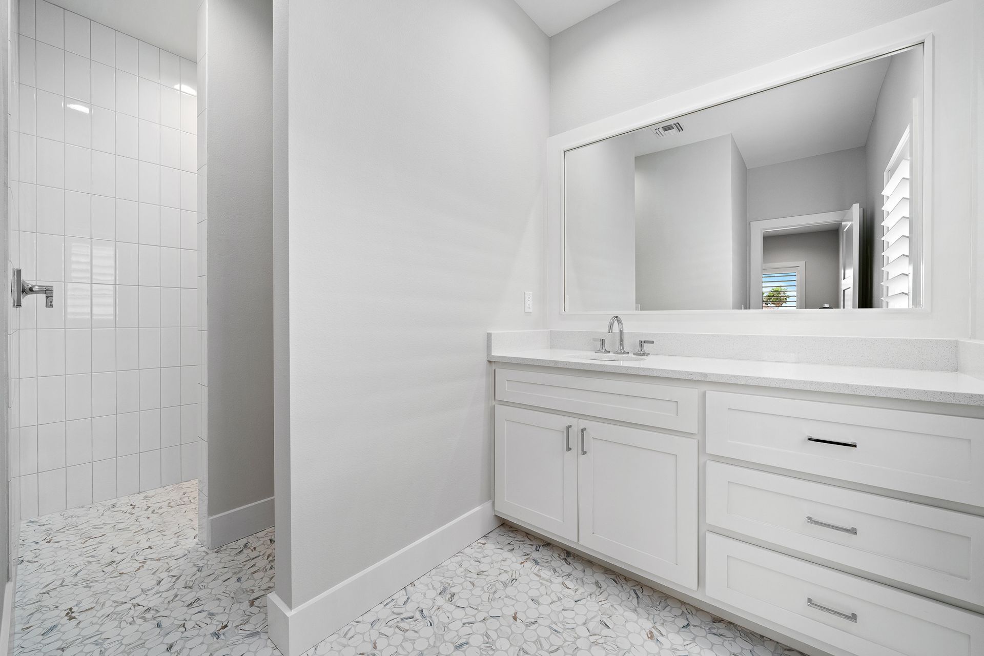 A bathroom with white cabinets , a large mirror and a walk in shower.