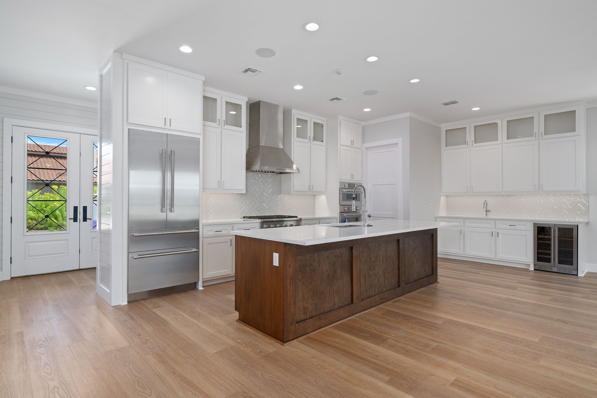 A kitchen with white cabinets , stainless steel appliances , a large island , and hardwood floors.