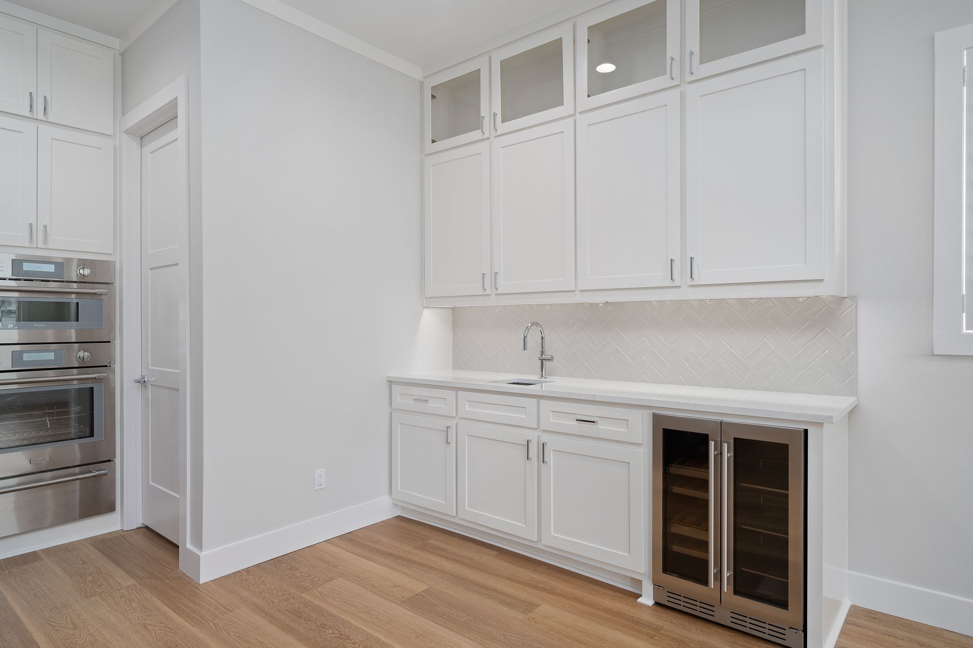 A kitchen with white cabinets , stainless steel appliances , a sink , and a wine cooler.